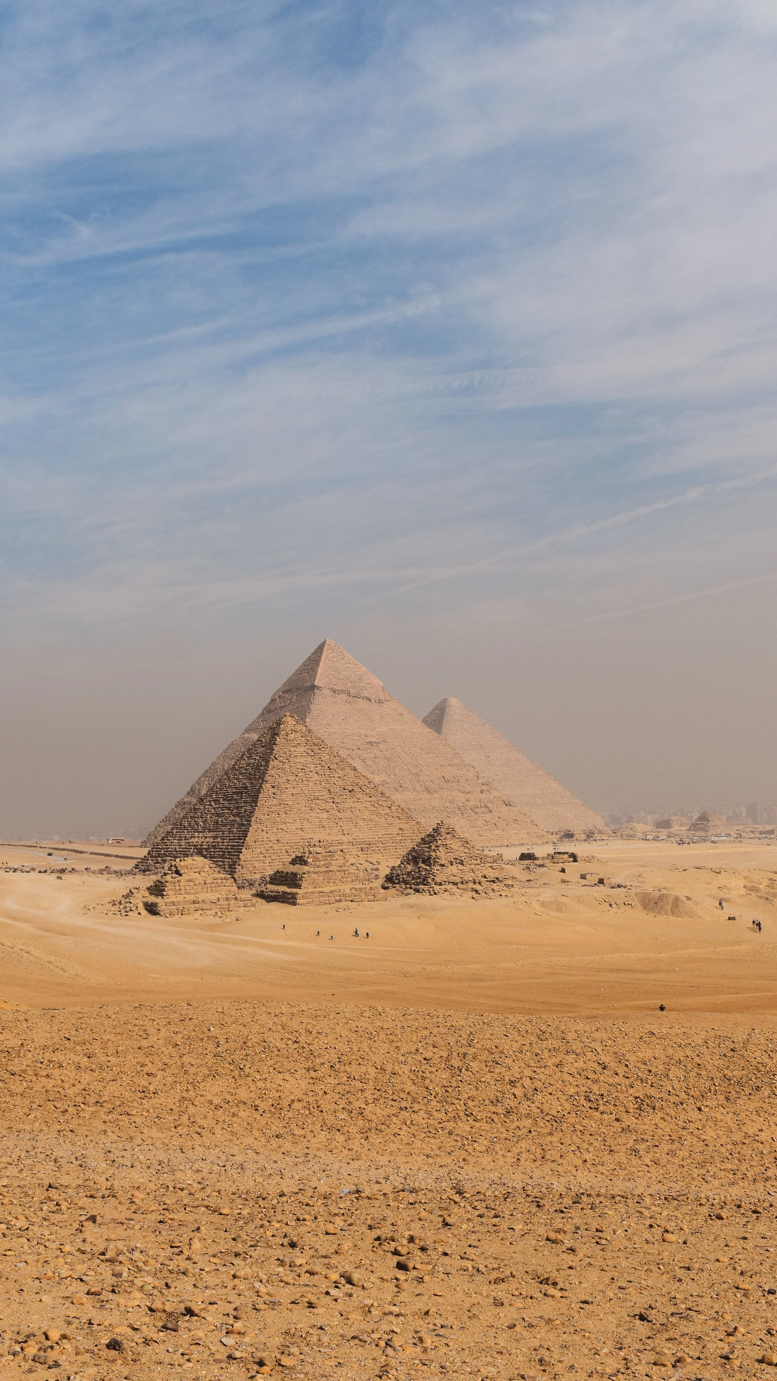 Three pyramids in a desert landscape under a partly cloudy sky.