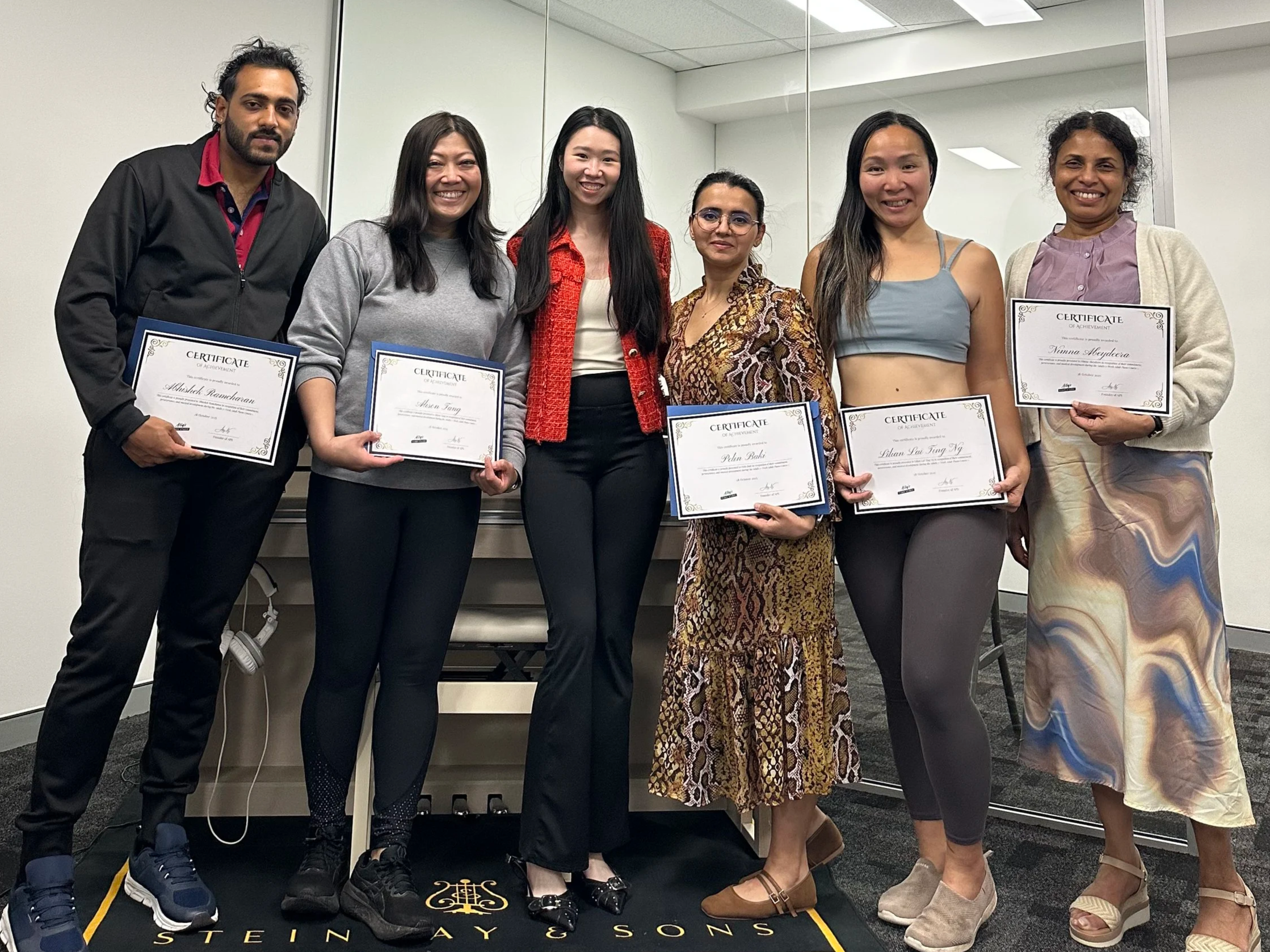A group of adult piano students smiling and holding their course completion certificates.