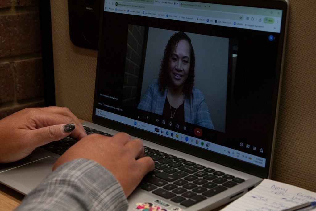 A person with painted nails wearing a plaid shirt using a laptop for a video call with a woman on the screen who has curly hair and is smiling.