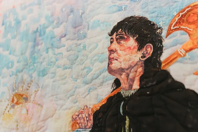 Quilted portrait by Sarah-Joy Ford depicting a figure holding a tool against a pale blue sky background.