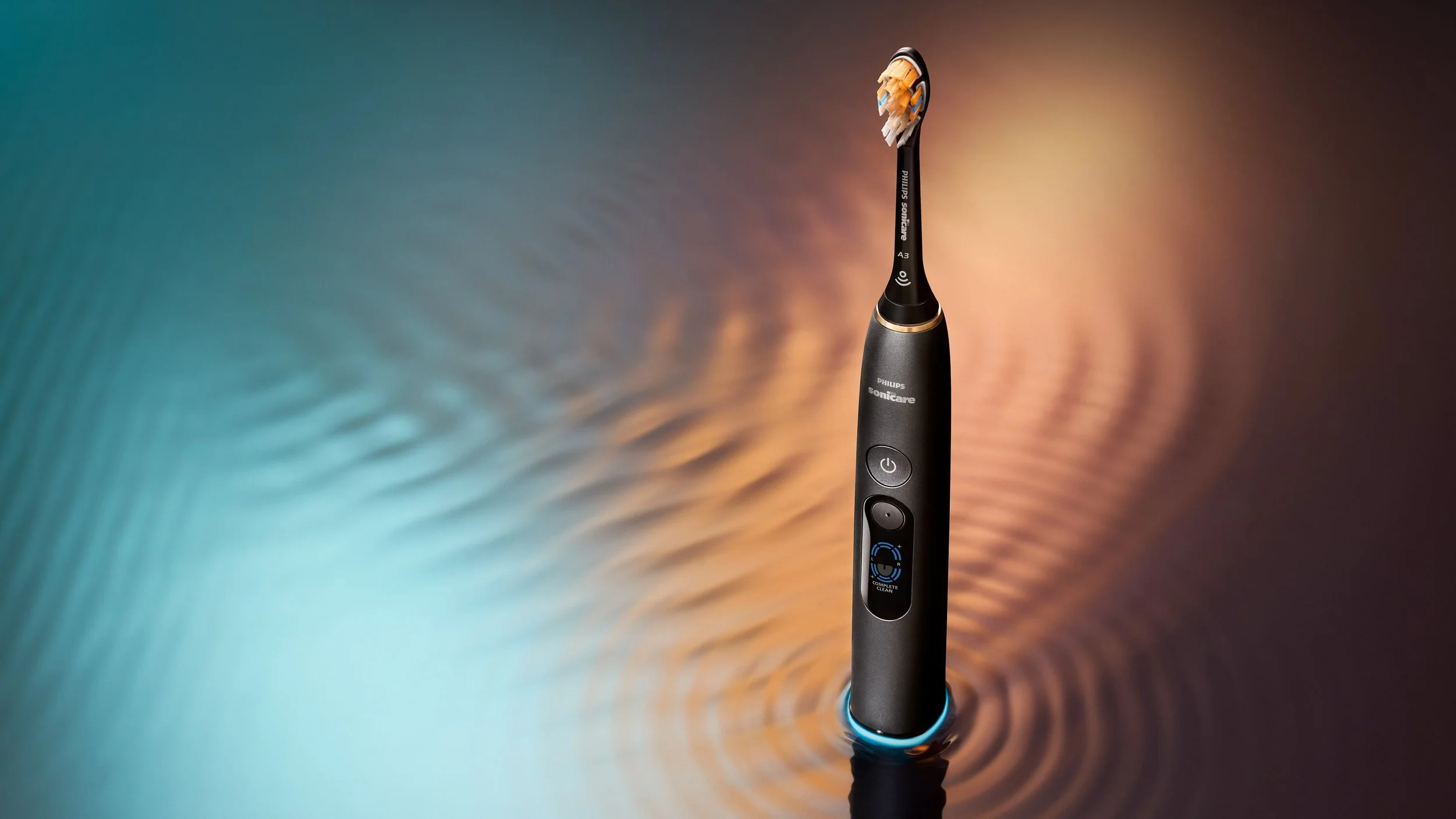 Black Philips Sonicare electric toothbrush standing upright on a reflective surface, surrounded by blue and warm orange light with circular ripple patterns. |

Philips Sonicare