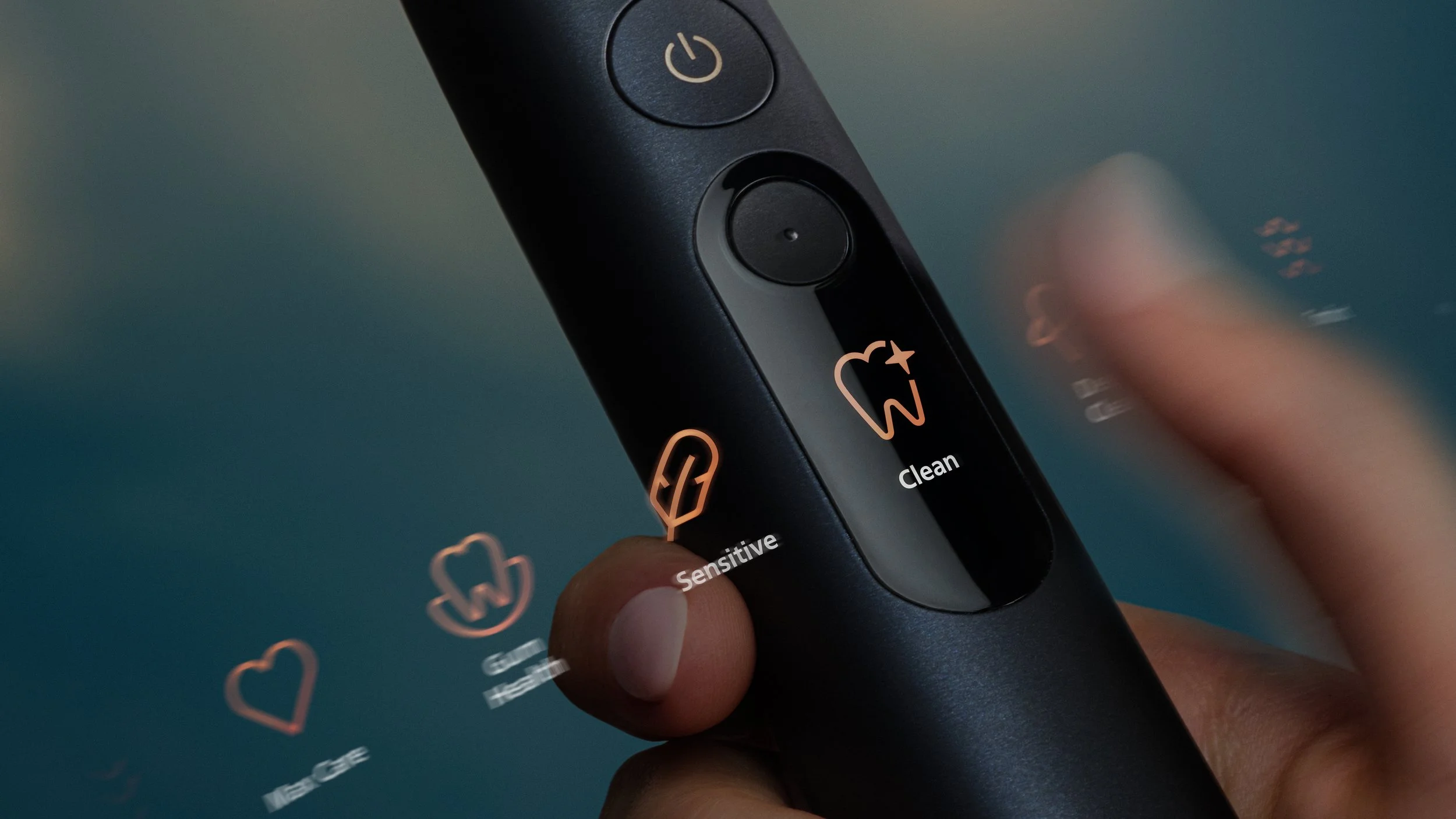 Close-up of a black Philips Sonicare electric toothbrush in hand, showing illuminated brushing modes and controls against a soft teal background. |

Philips Sonicare