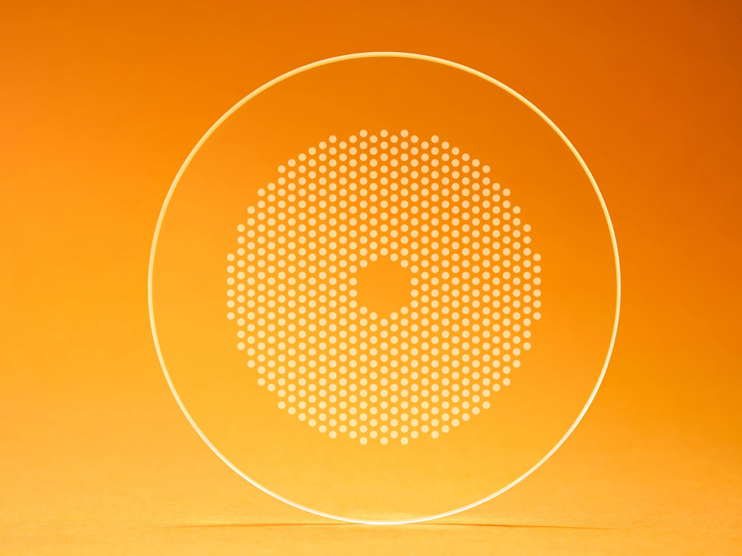 Close-up of a transparent MiYoSmart lens with a circular white dot pattern, photographed against a warm orange background. |

Hoya Miyo Smart