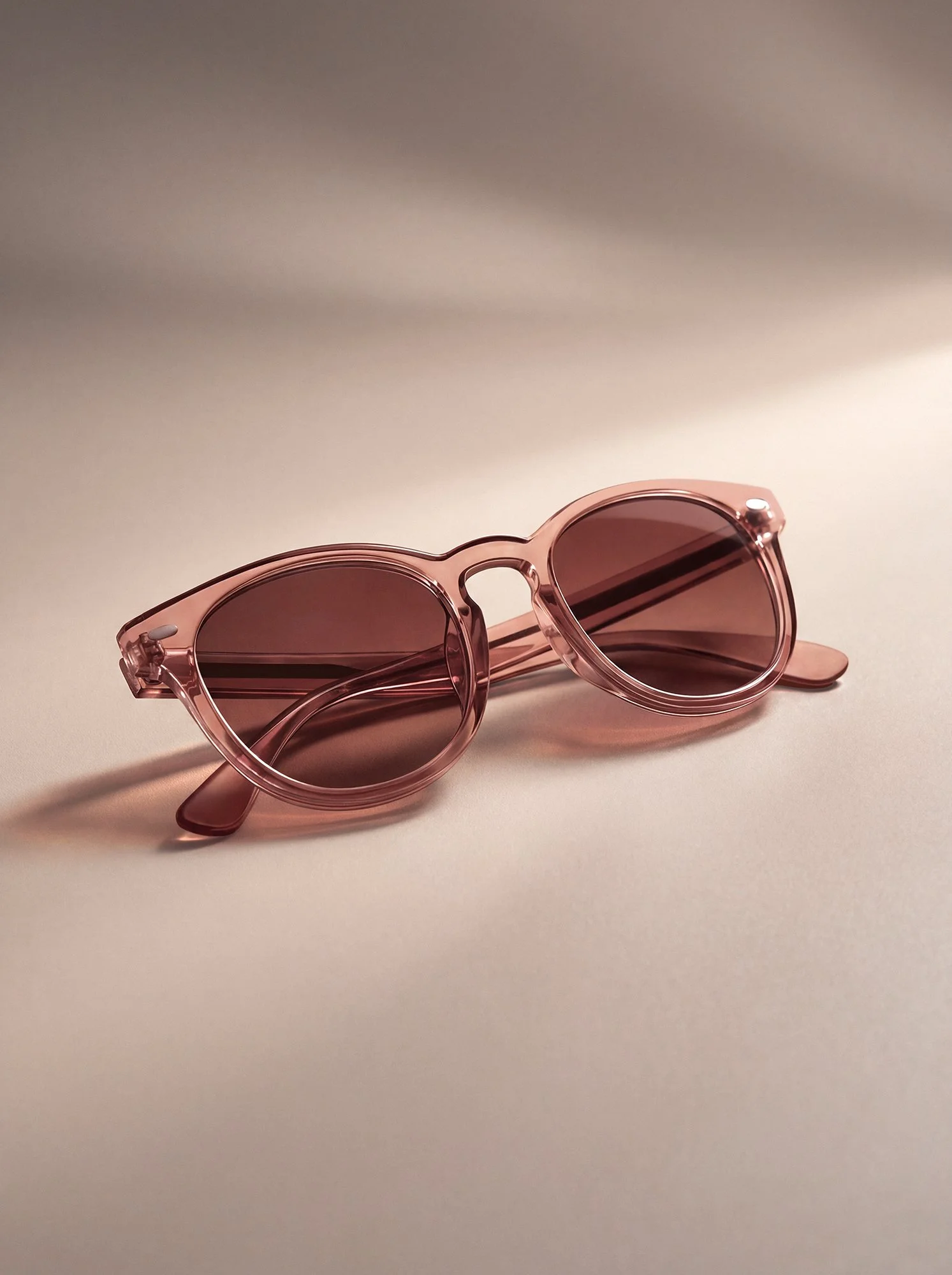 Transparent pink sunglasses with tinted lenses on a neutral background, AI-generated product image refined with professional Photoshop retouching and color grading.
