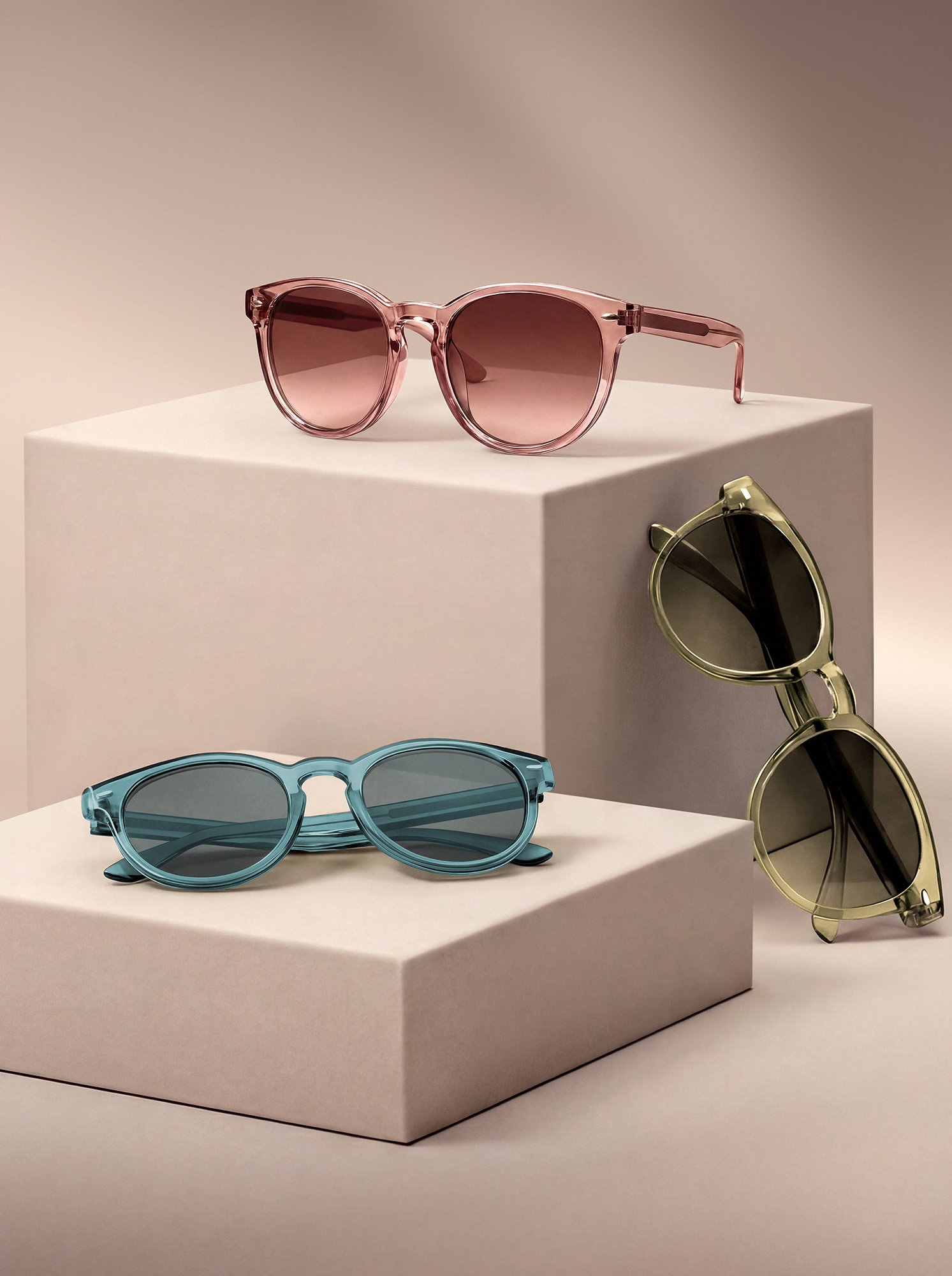 Collection of colorful sunglasses displayed on minimalist blocks in a studio setting, AI-generated visual enhanced with Photoshop retouching and color adjustments.