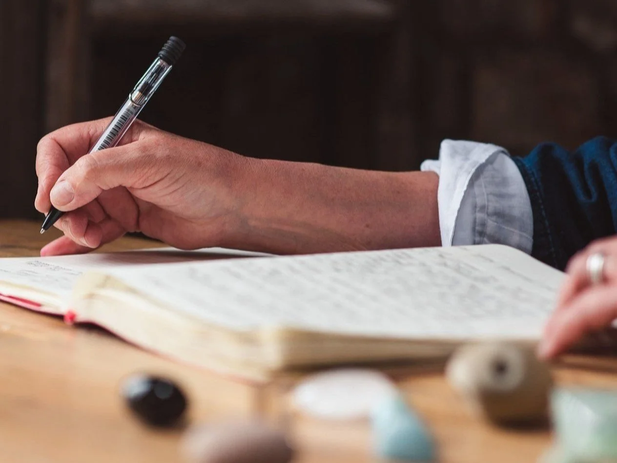 An arm and hand holding a pen, writing in a journal