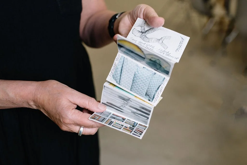 Close up of Jane Willis in a creative reflective practice workshop holding a little book of inspiration, which is a foldout zine with reflective writing, drawings and collages.