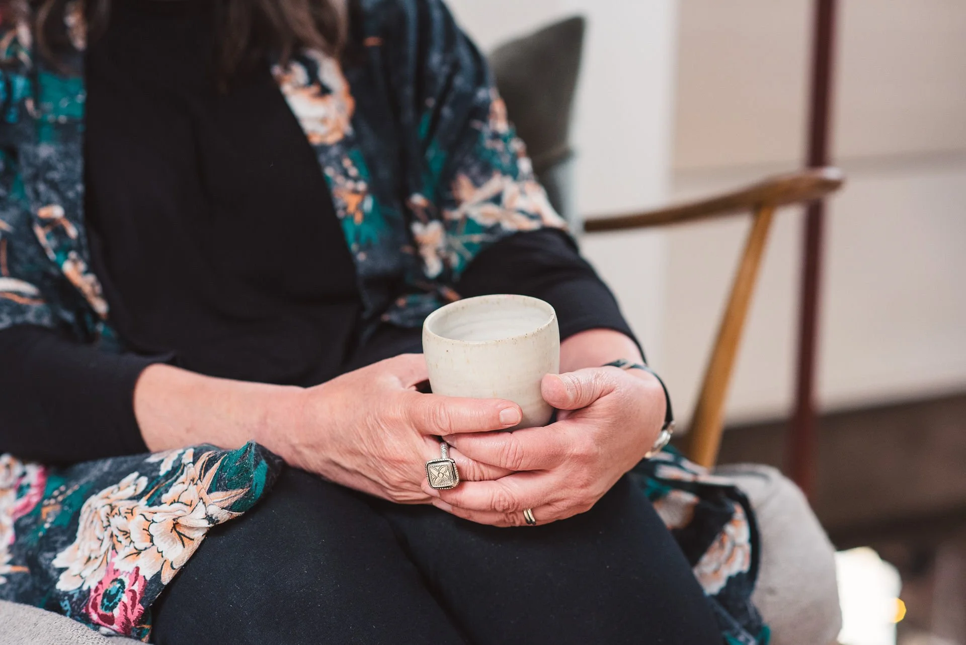 A close up shot of the hands of a white woman holding an earthenware cup. The pose is relaxed and welcoming, as if listening during a coaching sessions