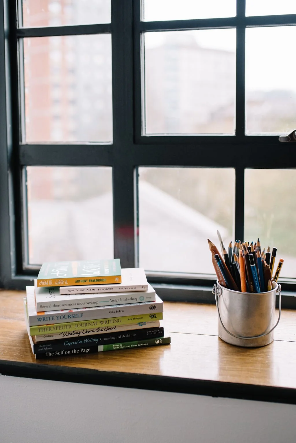 A window shelf with reflective tools on it, including a pot with pencils and a stack of books on reflective writing
