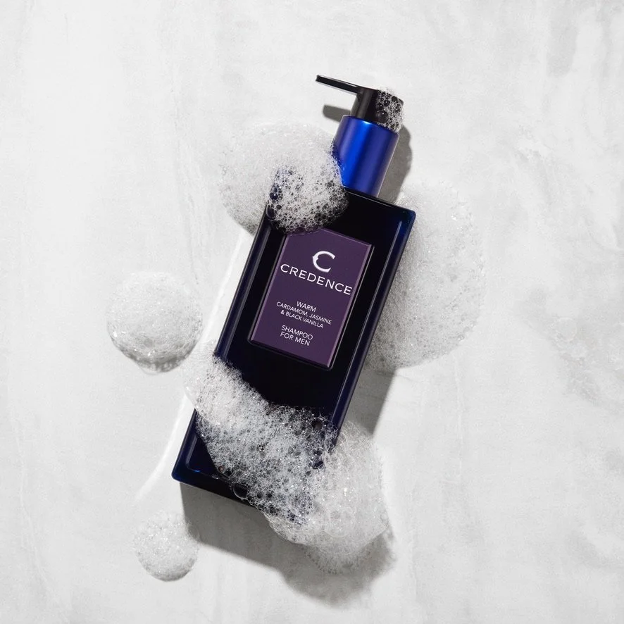 Blue bottle of Credence warm shampoo for men, surrounded by soap suds on a white surface.
