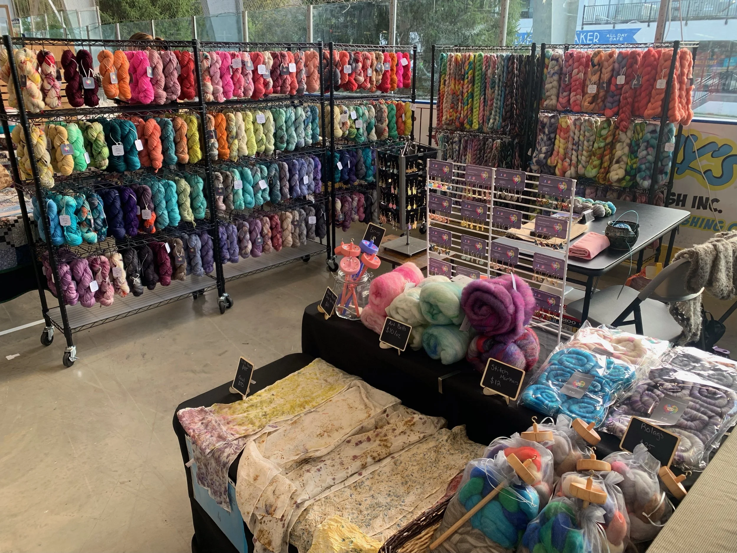 Picture of the Sheep on the Rainbow booth at Western NY Fiberarts Festival 2025. The picture has yarn and spinning fiber in every color.