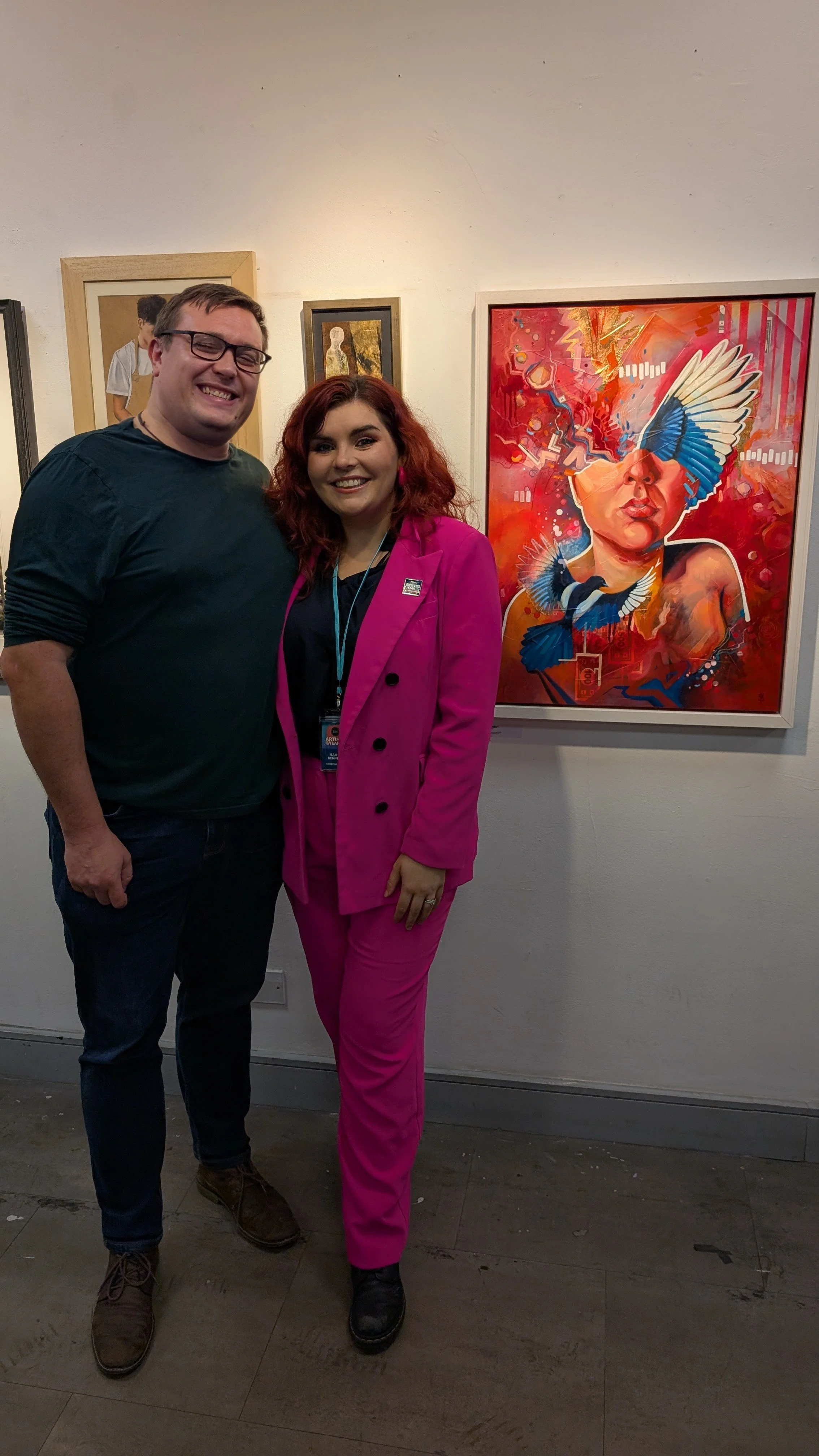 Surrey artist Sam B. Kennedy and her husband smiling beside Fortune Flames at the SAA Artist of the Year 2026 finalists exhibition, held at the Cass Art Space in Kingston.