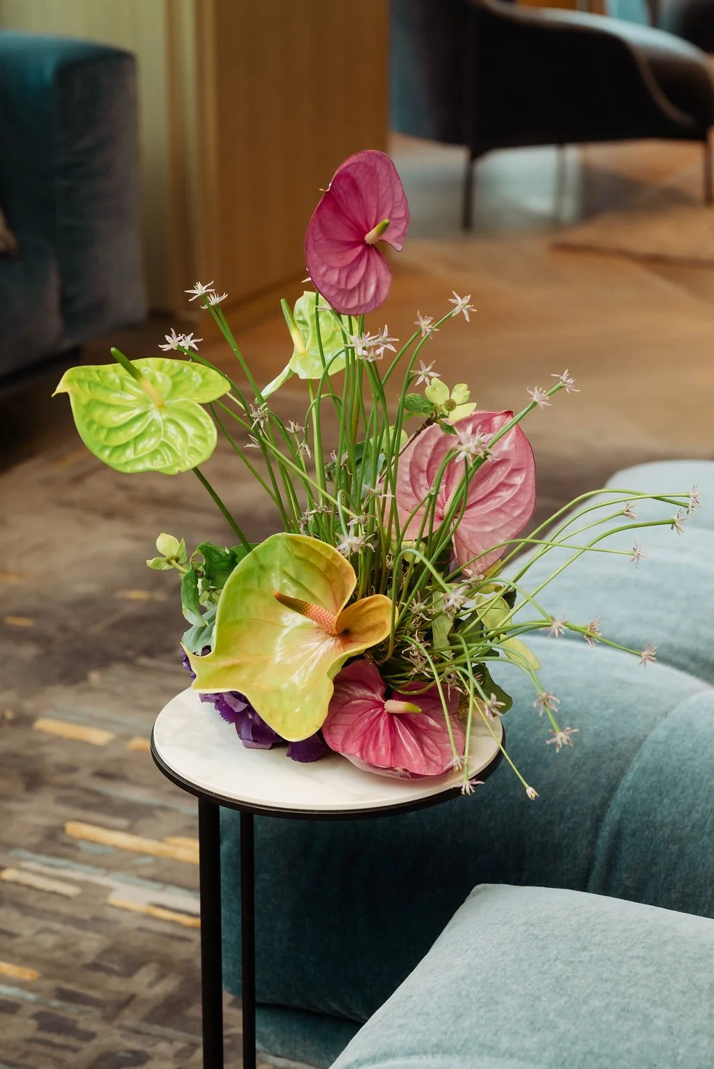 Modern colorful arrangement of anthuriums and small white flowers on a small round table in a cozy living room.