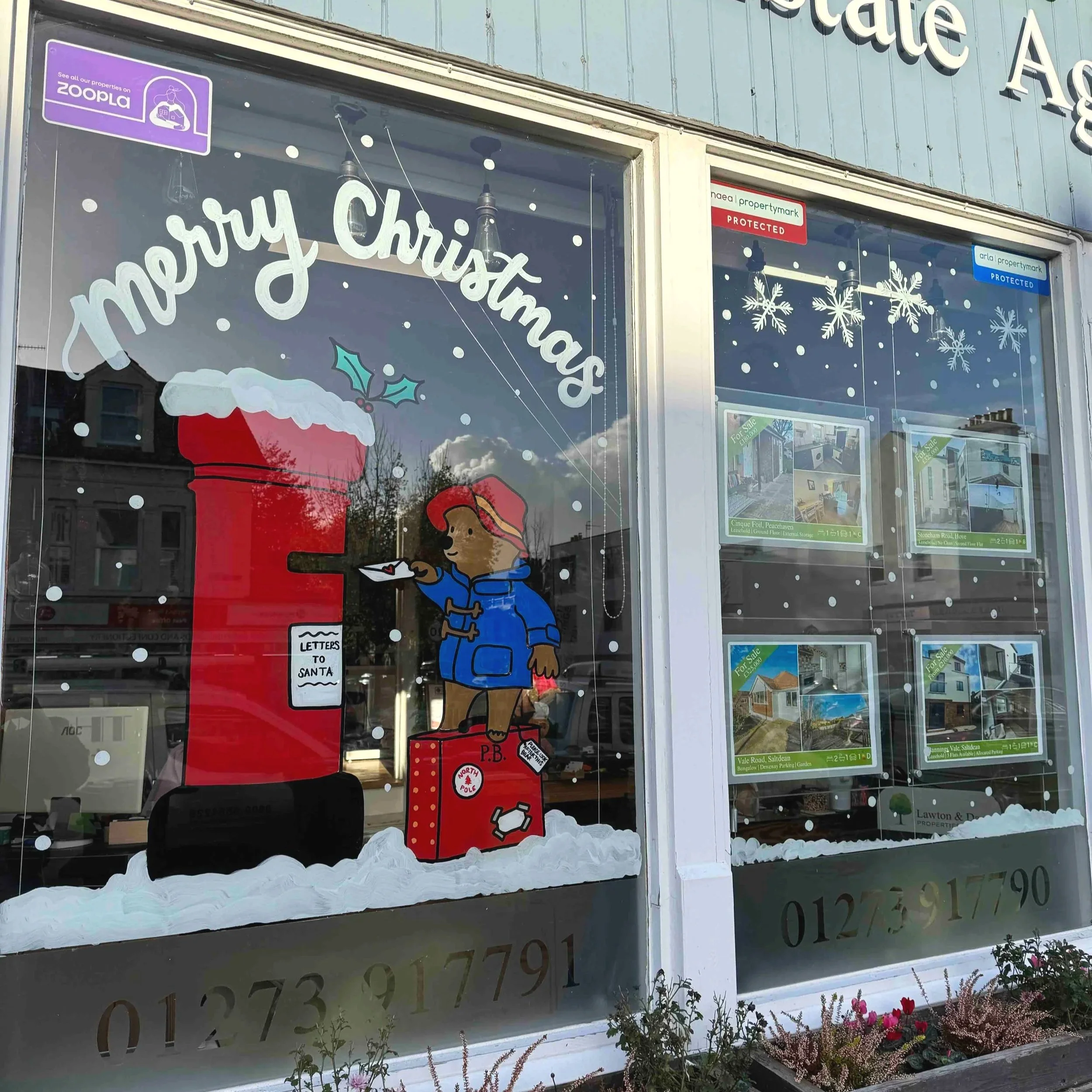 Hand-painted paddington in an estate agent window. He is posting a letter to santa, standing on his briefcase.