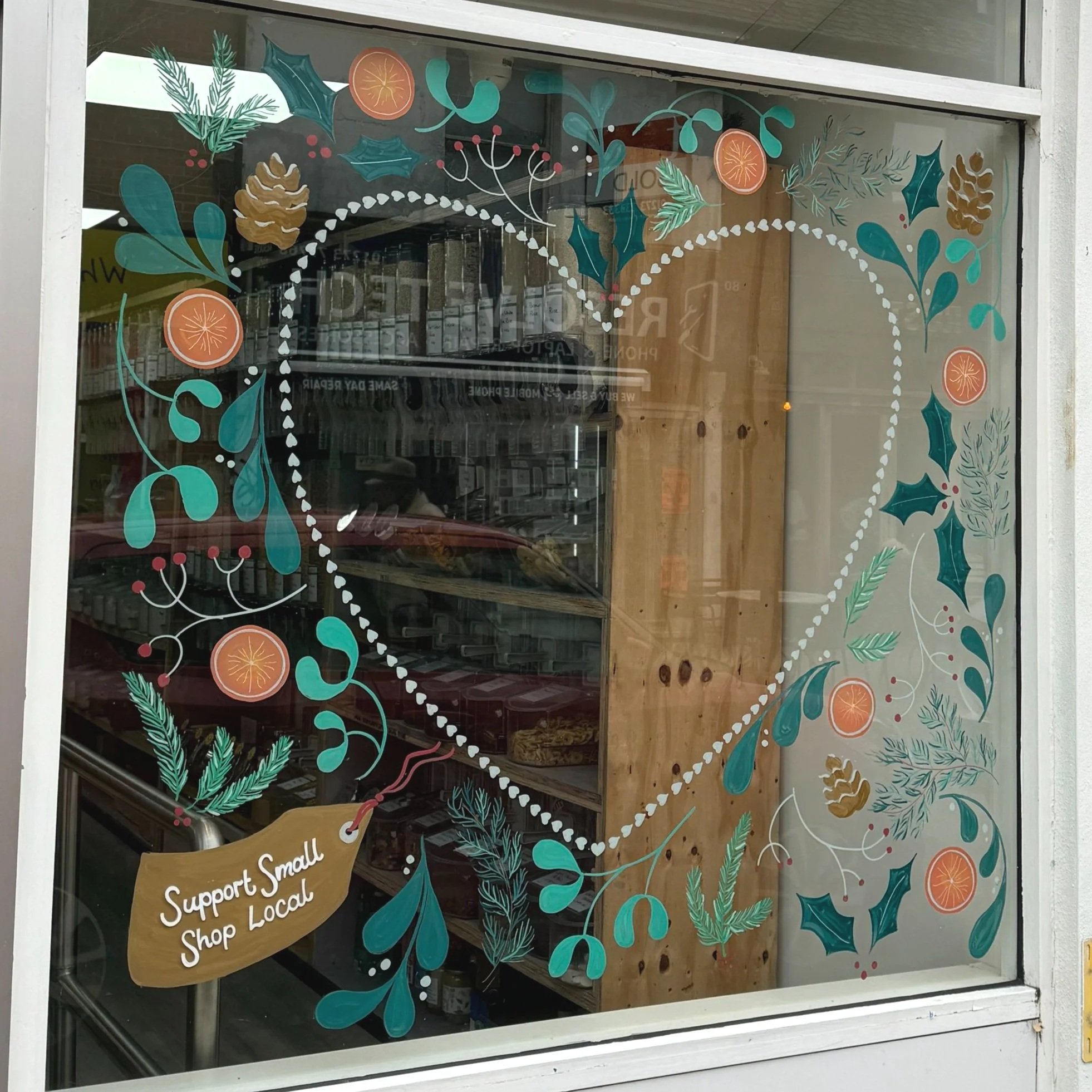 Christmas window featuring a heart shaped frame surrounded by festive leaves and a label that says support small shop local