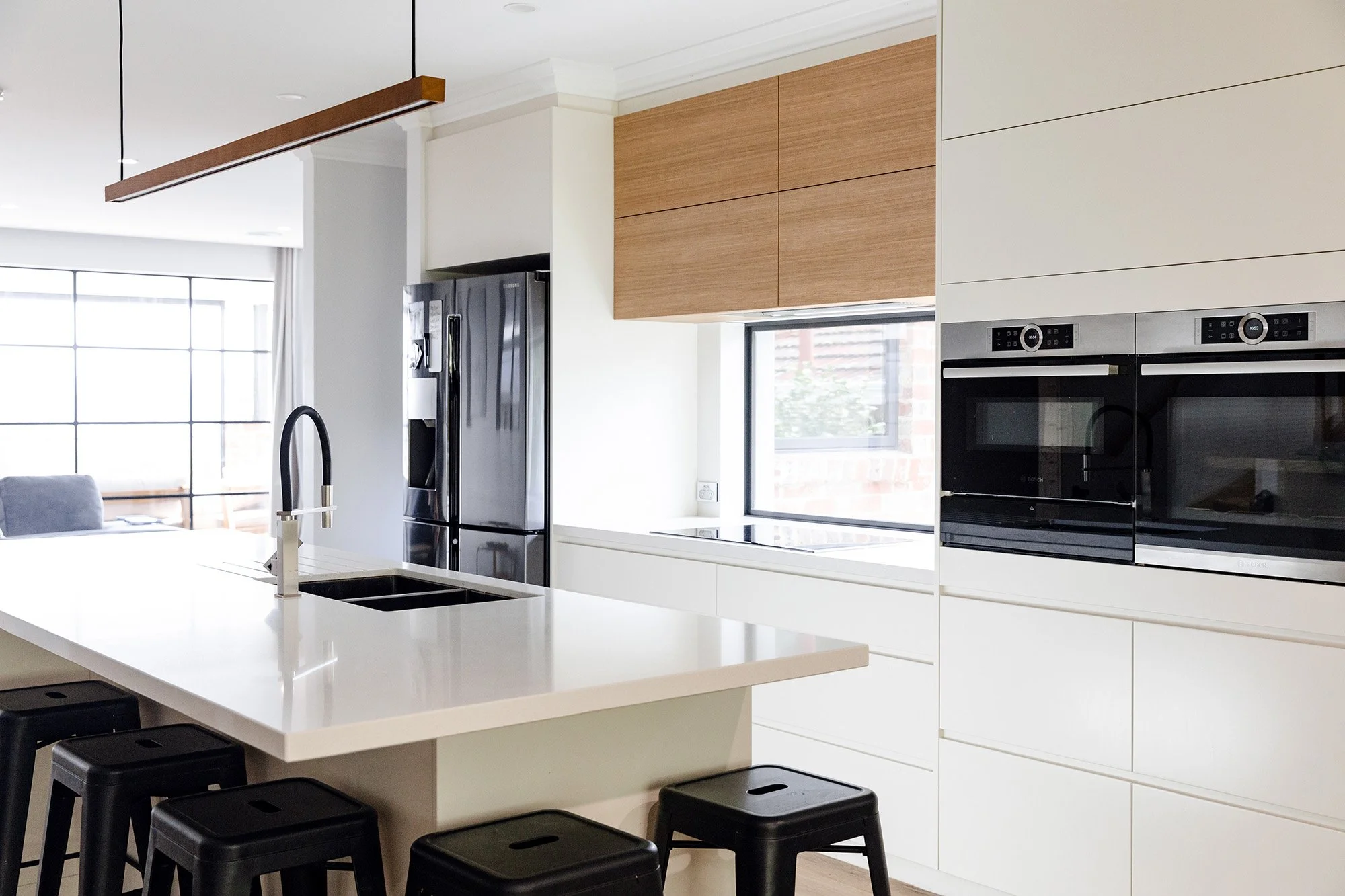 Modern kitchen with a white countertop, a potted peace lily plant, and wooden and white wall cabinets with decorative items.