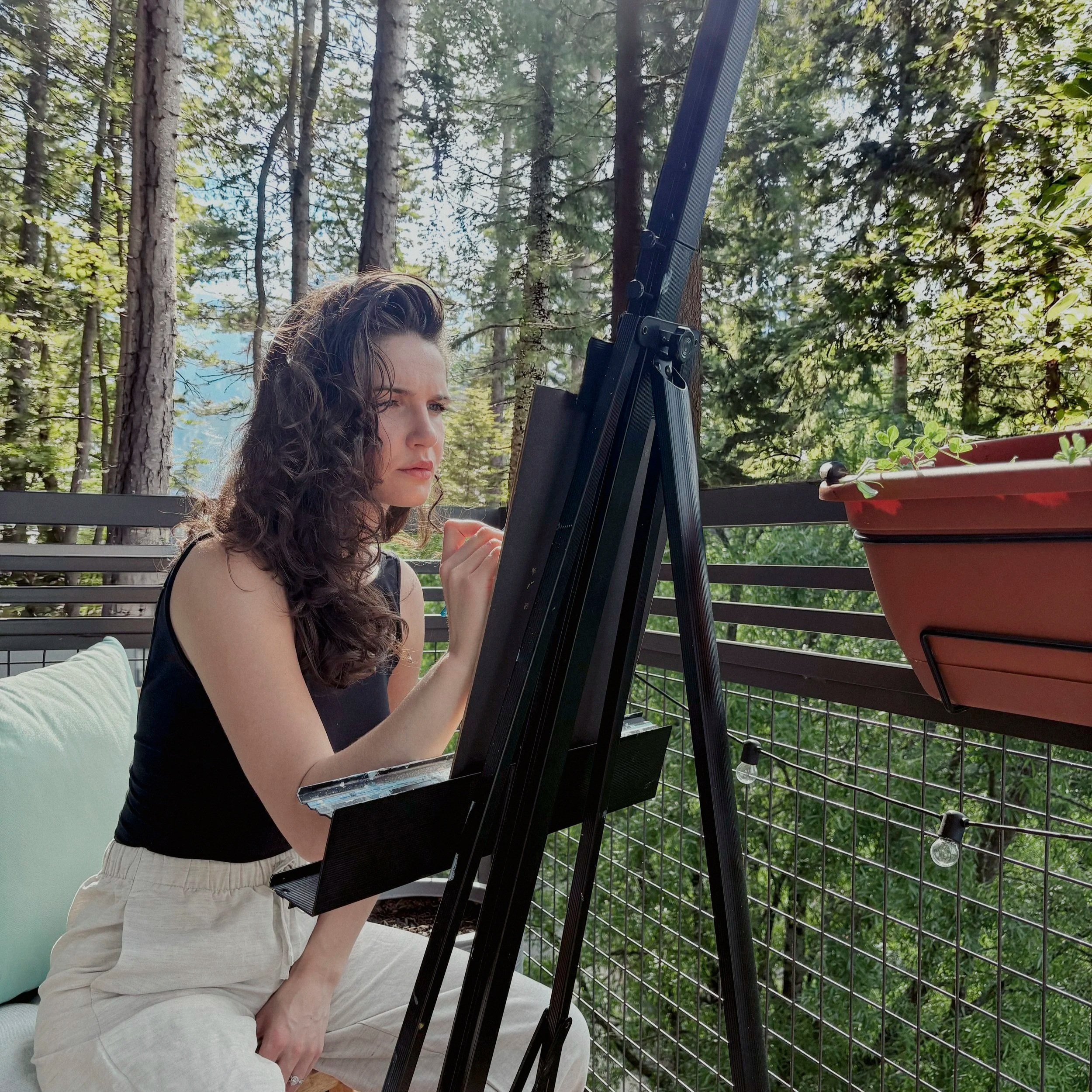 Brooke Eastgate owner of BE Landscape Artist Inc. painting outdoors on balcony with trees in background