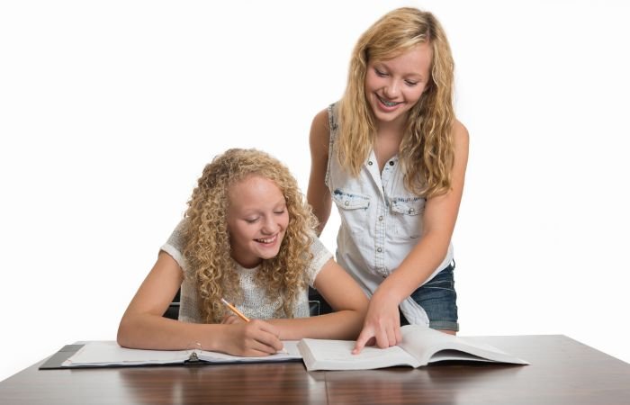Two girls sitting at a desk, focused on a book during a college counseling session.
