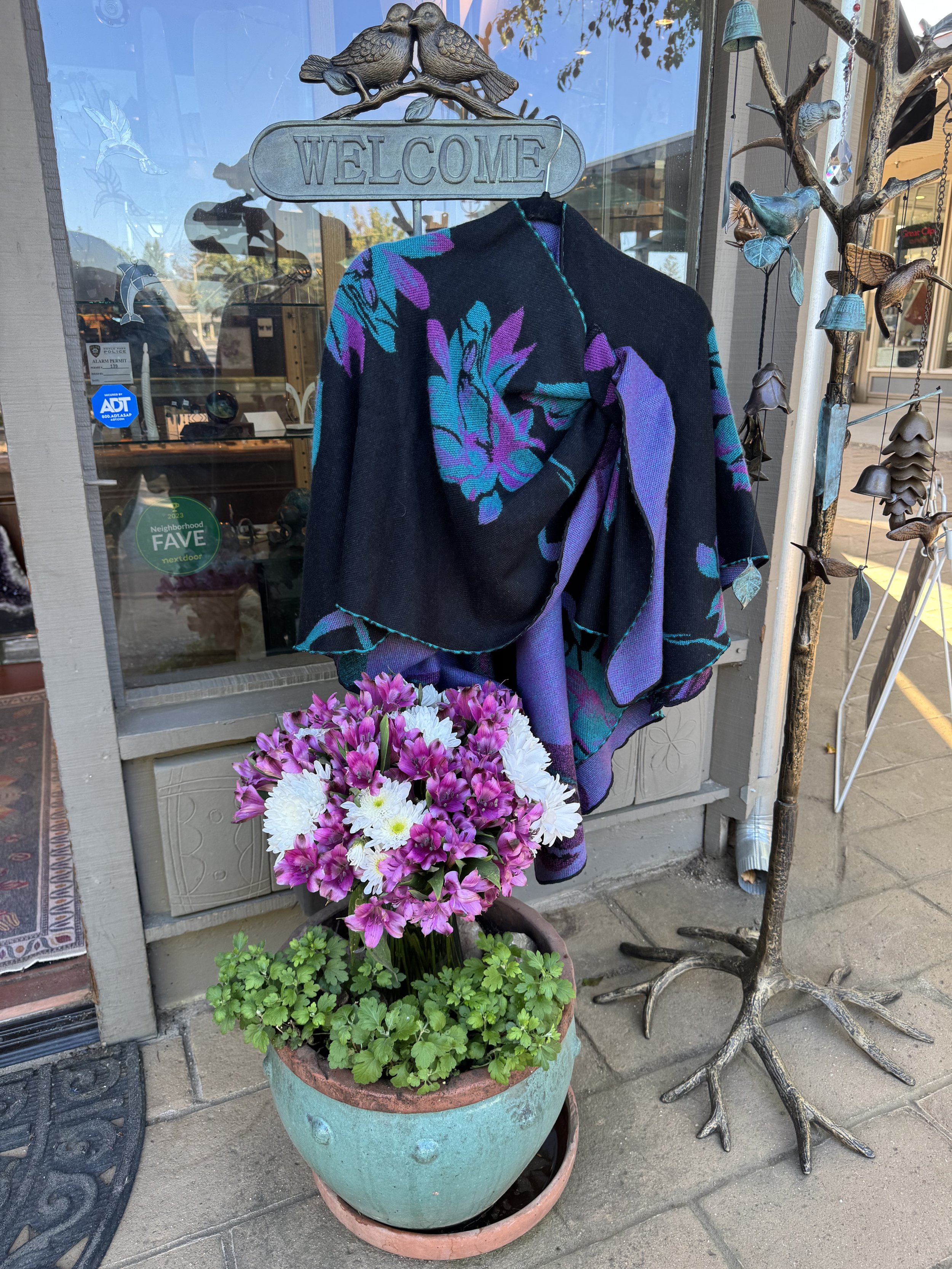 A photo of our ever popular reversable loop shouldered shawl in a new color way, taken outside our store. Thank you Gabe and Maria for helping with this photo shoot. And of course Maria for the beautiful flower arrangement in our colors!💜💙💜