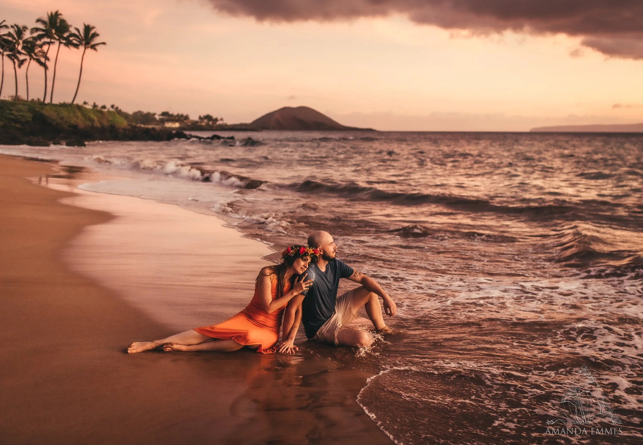woman sitting behind man in shoreline during sunset celebrating engagement with couples photos in maui, hawaii