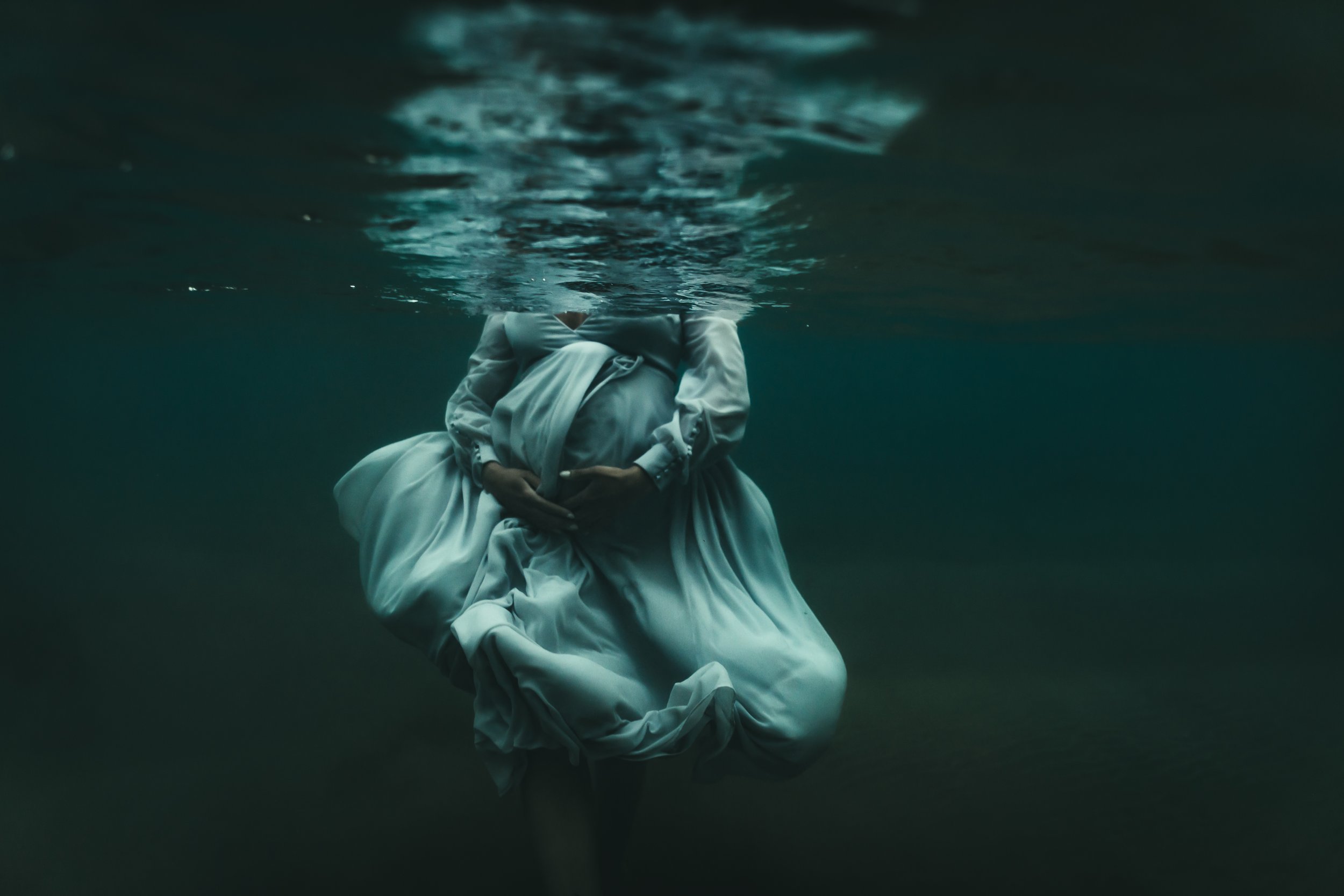 pregnant woman's tummy underwater in flowy dress holding tummy