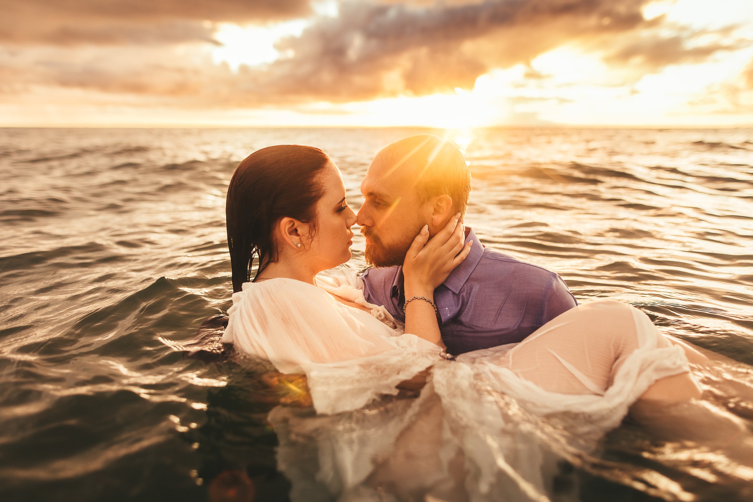 man carrying woman romantically in ocean as they gaze into eachothers eyes in maui hawaii