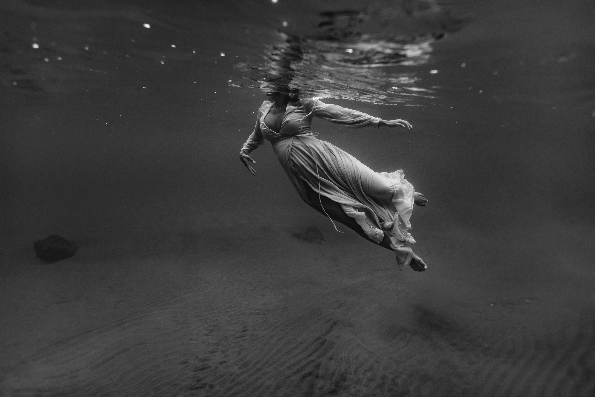 black and while underwater photo of pregnant woman in flowy dress swimming