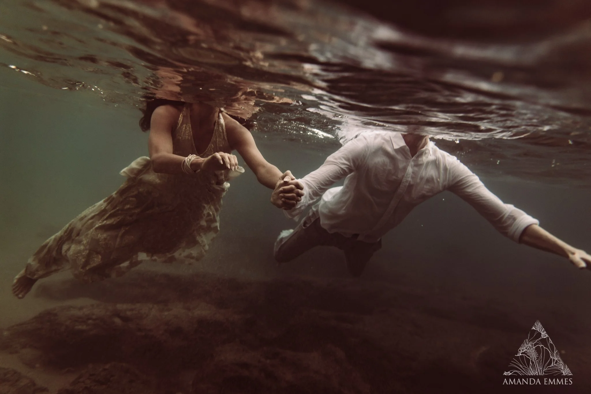 man and woman swimming underwater holding hands during a sunset engagement photo session in maui, hawaii