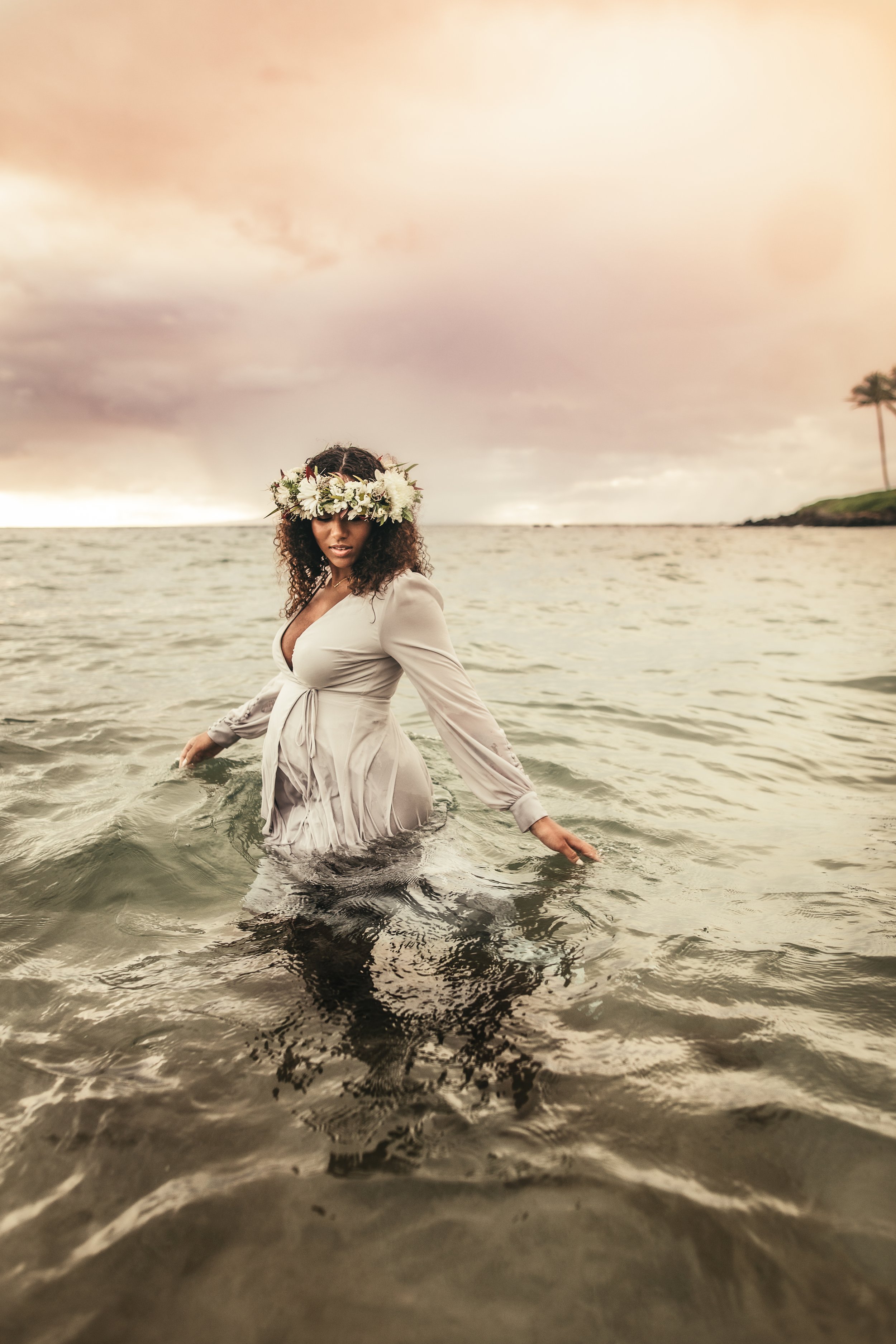 pregnant african american woman walking in ocean with flower crown during sunset in maui hawaii