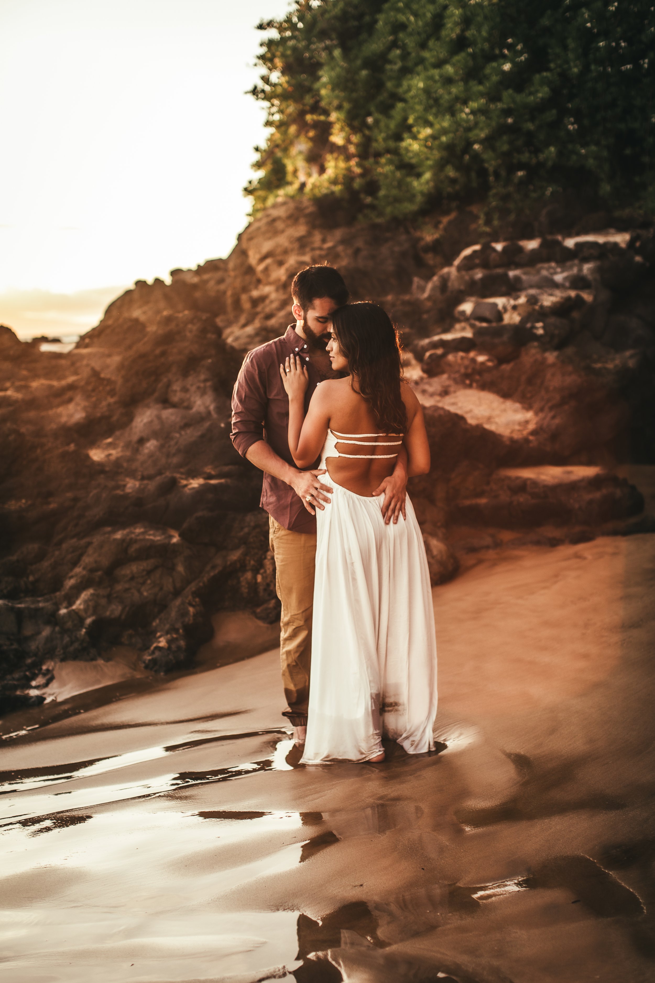 man and woman holding eachother as her back faces camera, while they look out into the ocean in maui hawaii