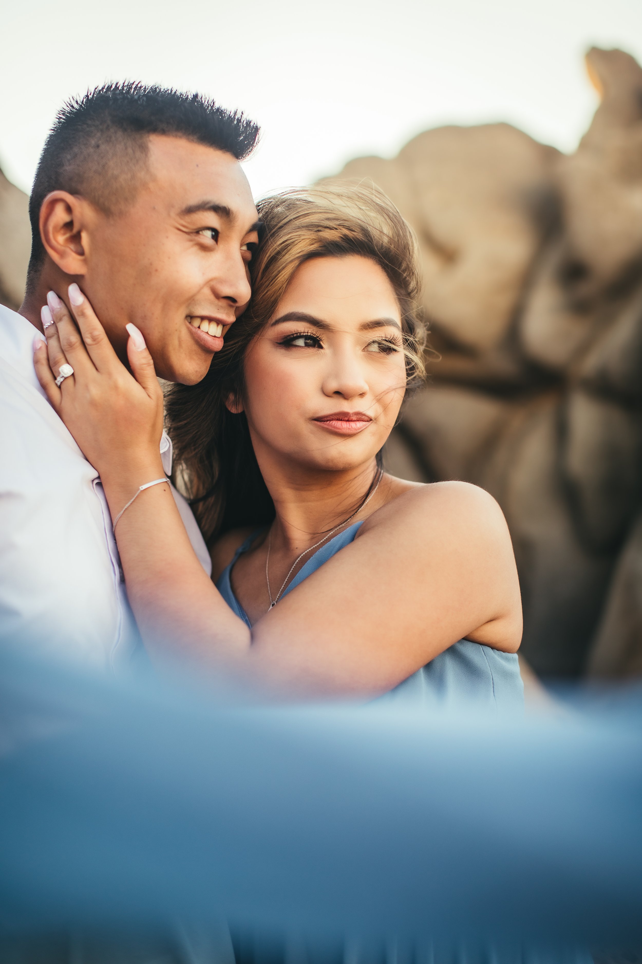woman in blue dress leaning into man with her hand on his cheek as they both gaze out to the ocean at ironwoods beach in kapalua maui