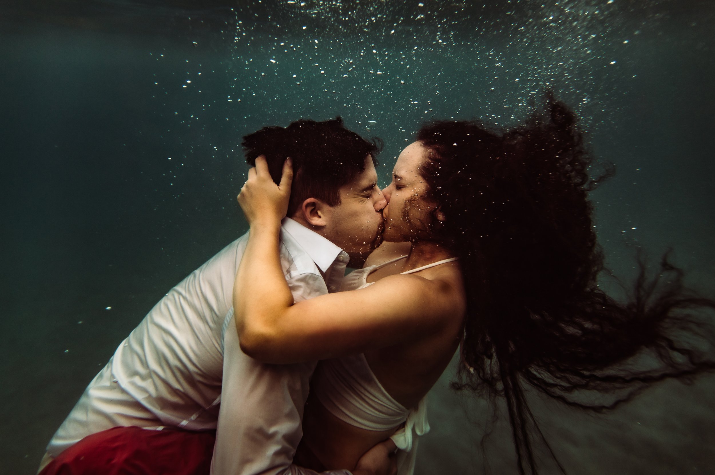 white man and african american woman kissing underwater in maui hawaii
