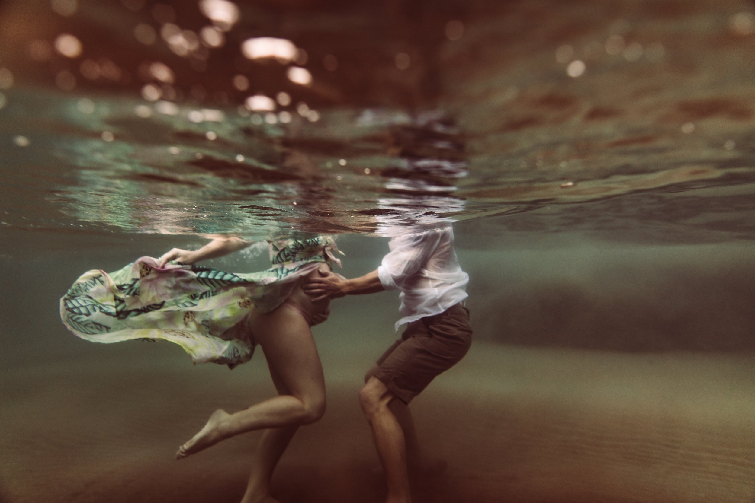 pregnant woman and man underwater from chest down, with hands on her tummy