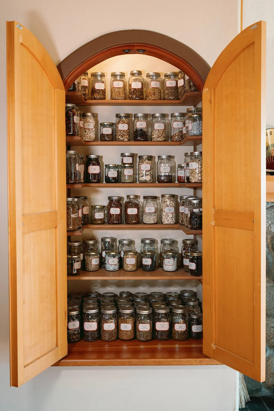 A wooden cabinet filled with glass jars containing various traditional chinese herbal medicine organized neatly on shelves.
