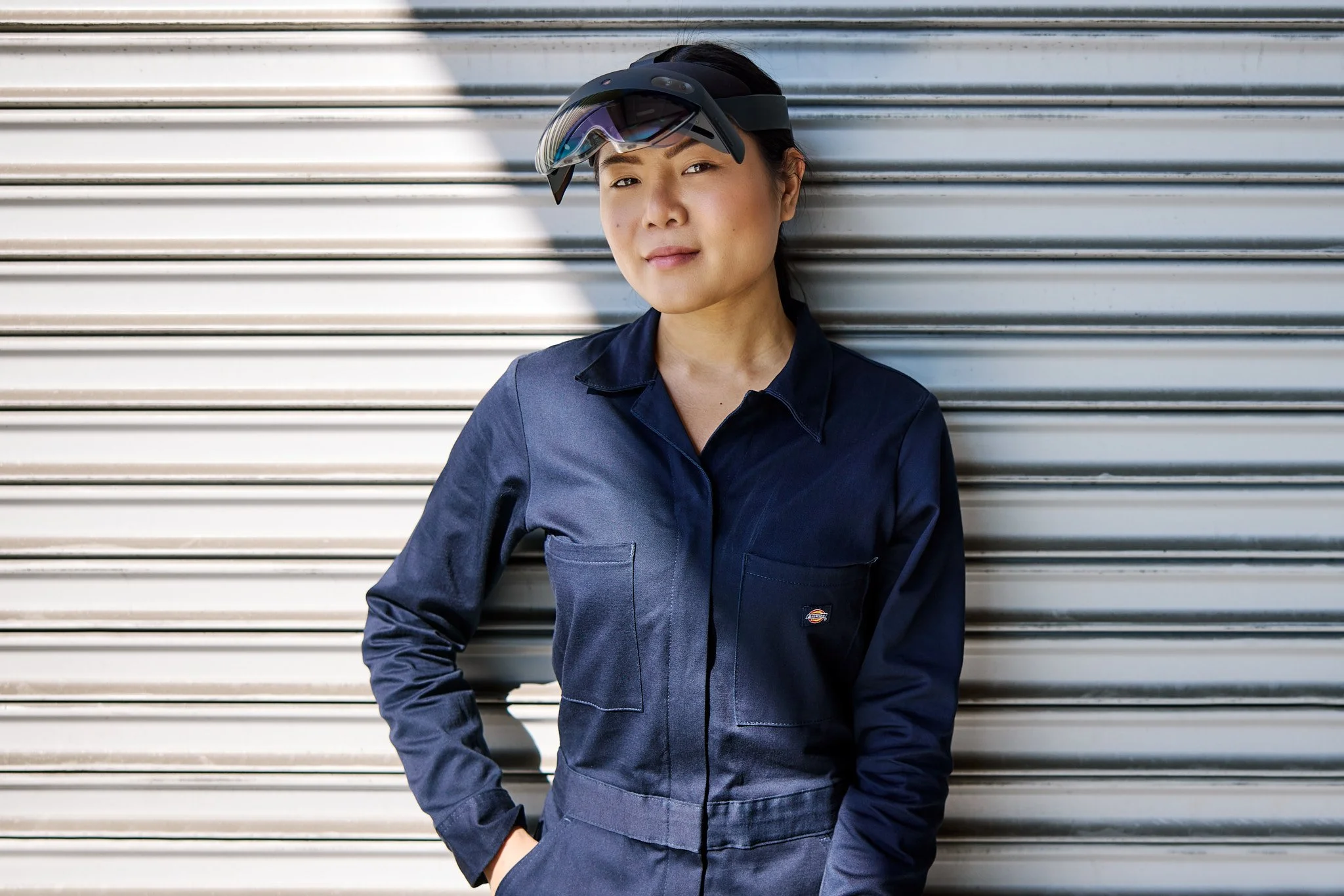 Woman wearing protective goggles and a navy blue work uniform standing against a metal roll-up door.