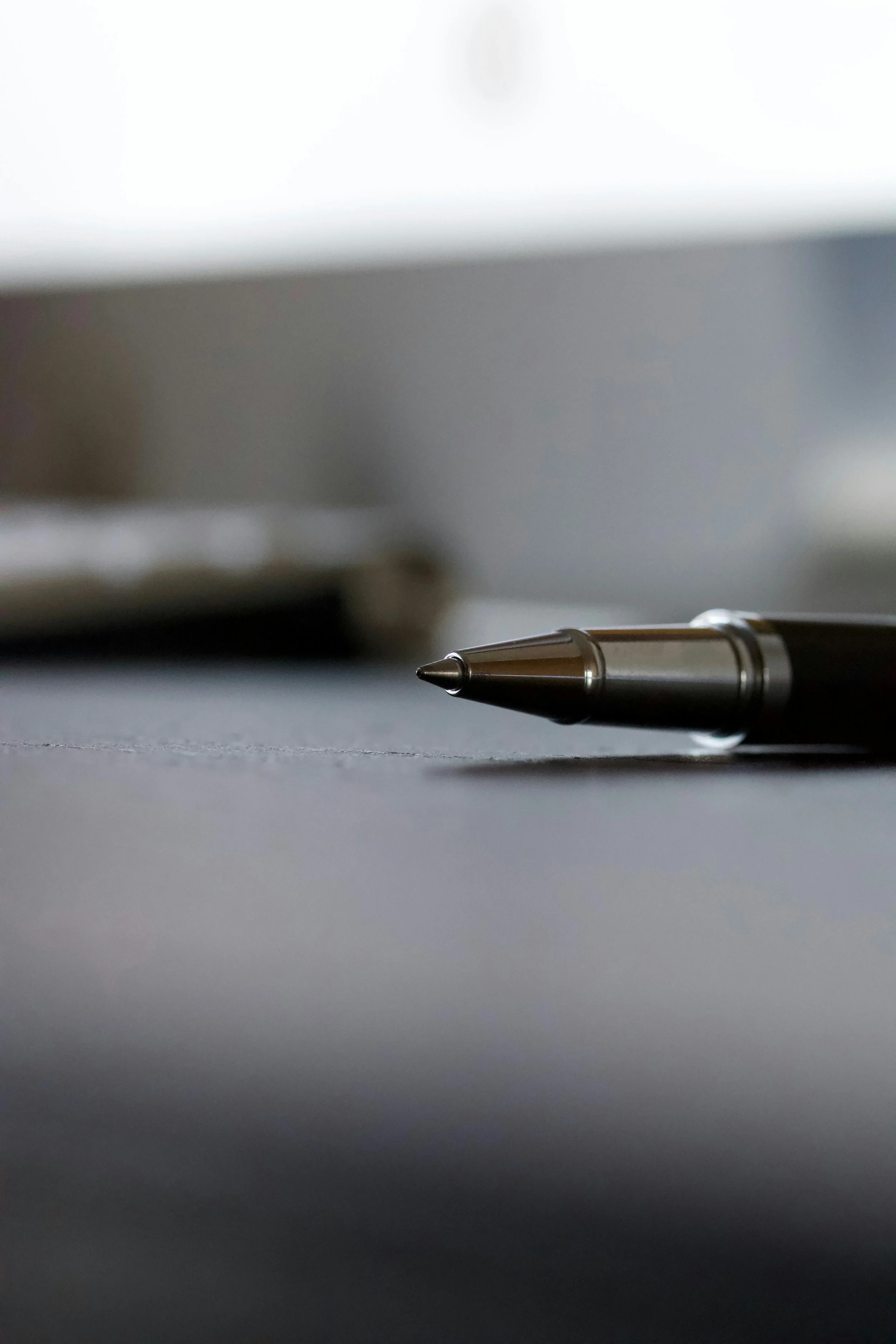 Close-up of a silver ballpoint pen resting on a grey surface with a blurred background.