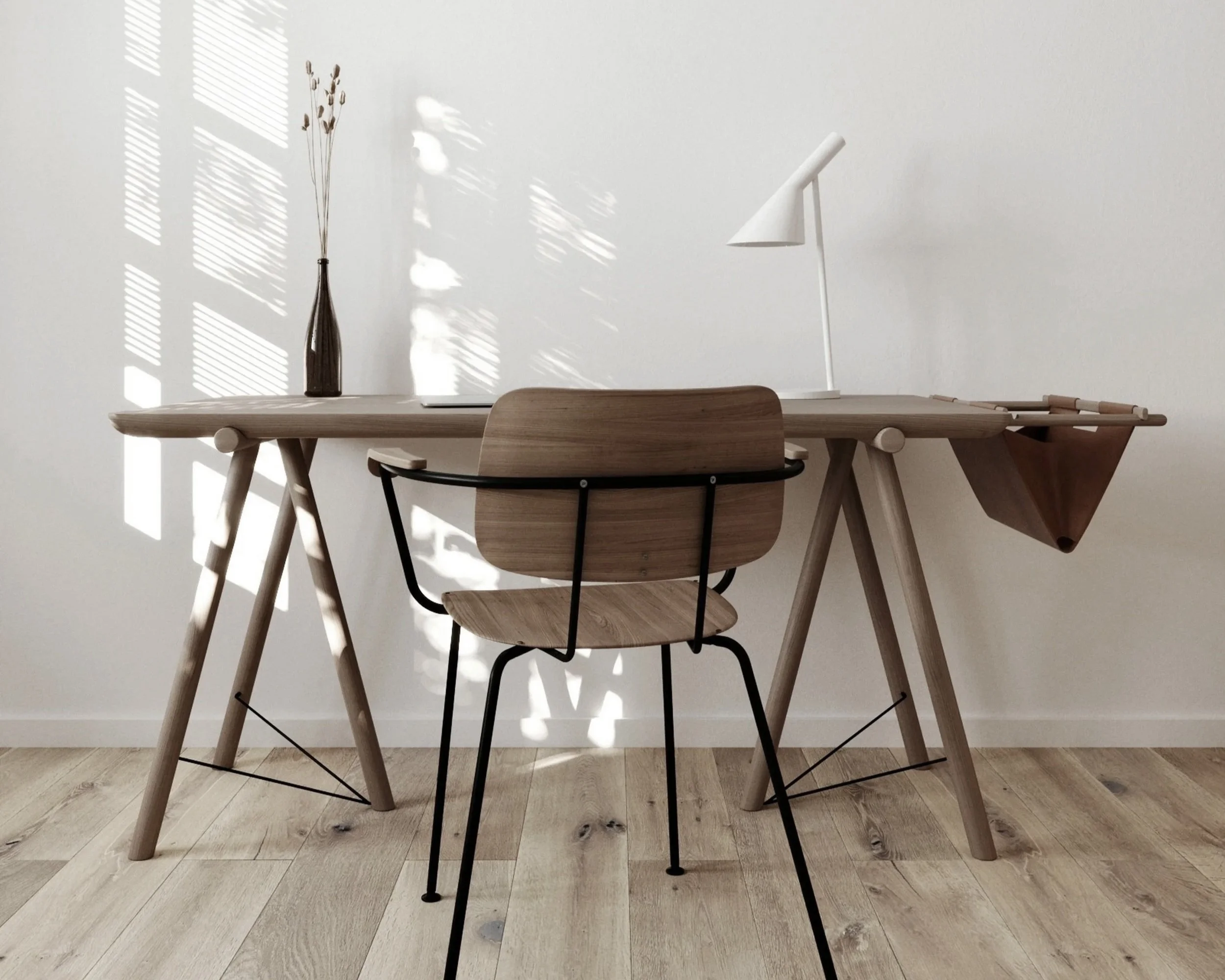 A minimalist wooden desk with a white desk lamp, a tall dark vase with dried plants, and a wooden chair with black metal legs, against a wall with sunlight and shadows from window blinds.