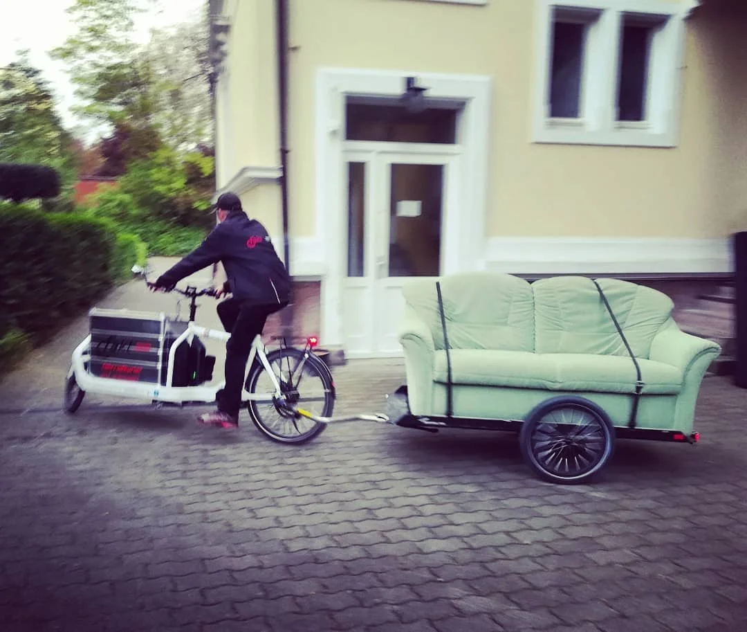 Radfahrer mit Boxenanhänger vor einem Wohnhaus