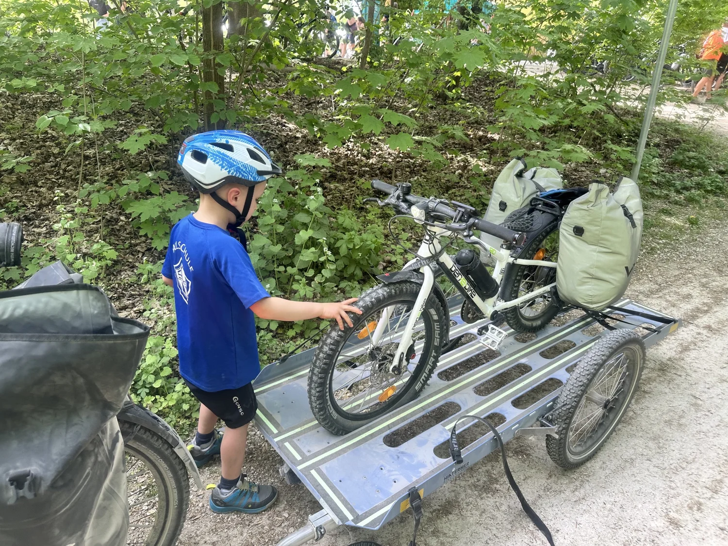 Kind schiebt sein Fahrrad auf den Hinterher Transporter, daneben ein Lastenrad