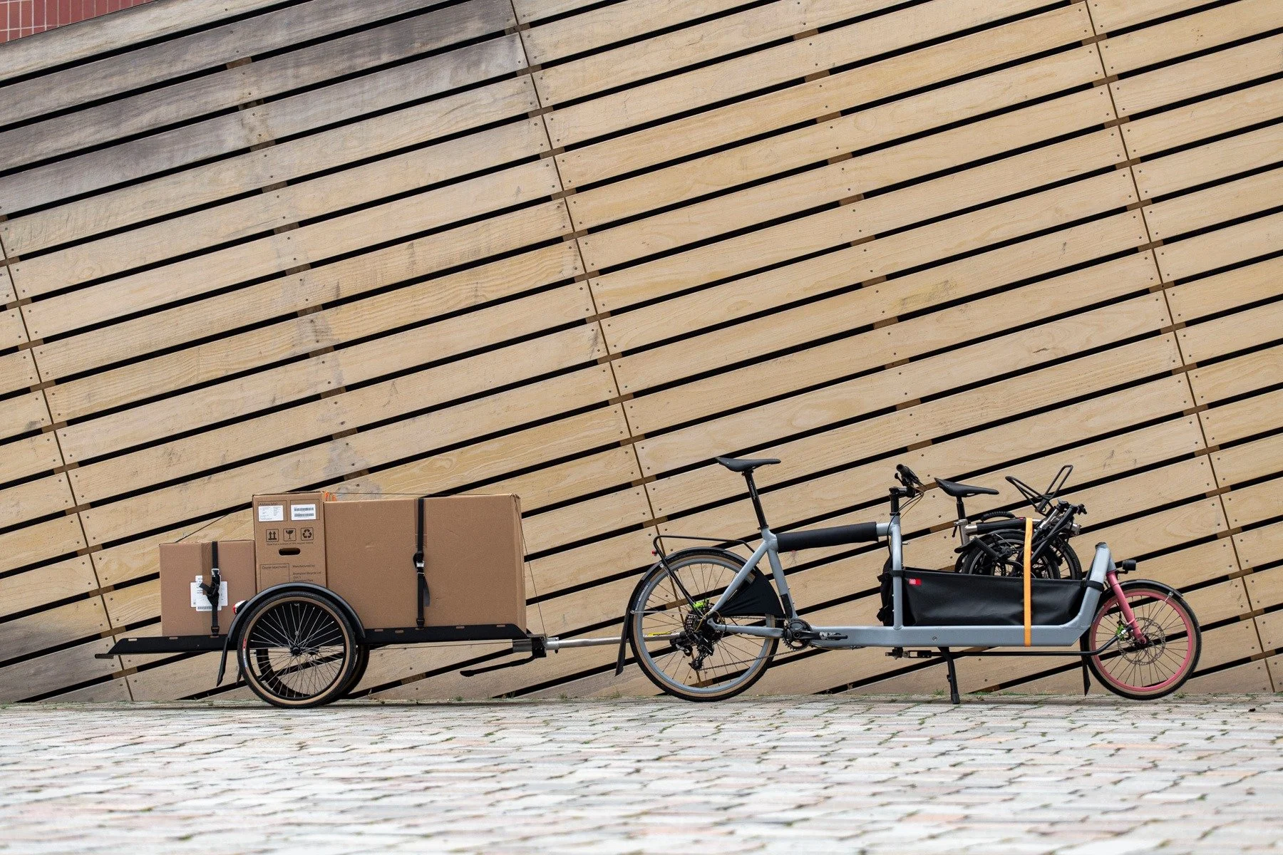 Lastenrad mit Fahrradanhänger vor einer Holzwand
