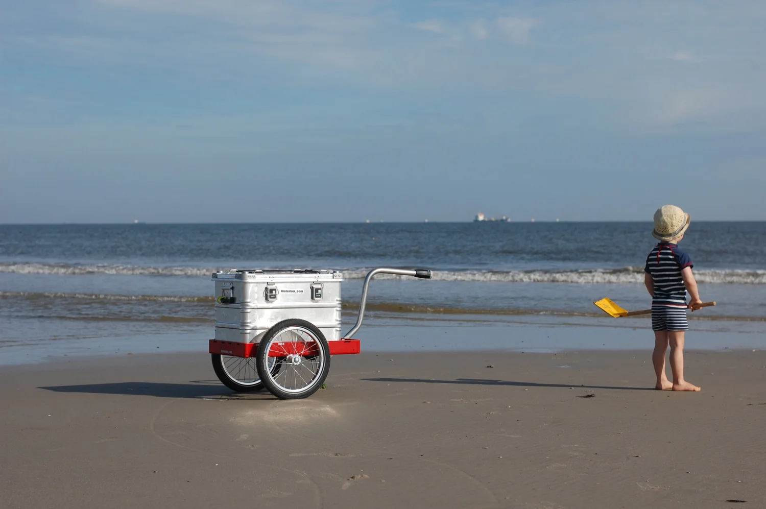 Kind am Strand von Wangerooge, daneben ein Hinterher Hmini mit Alubox als Handwagen