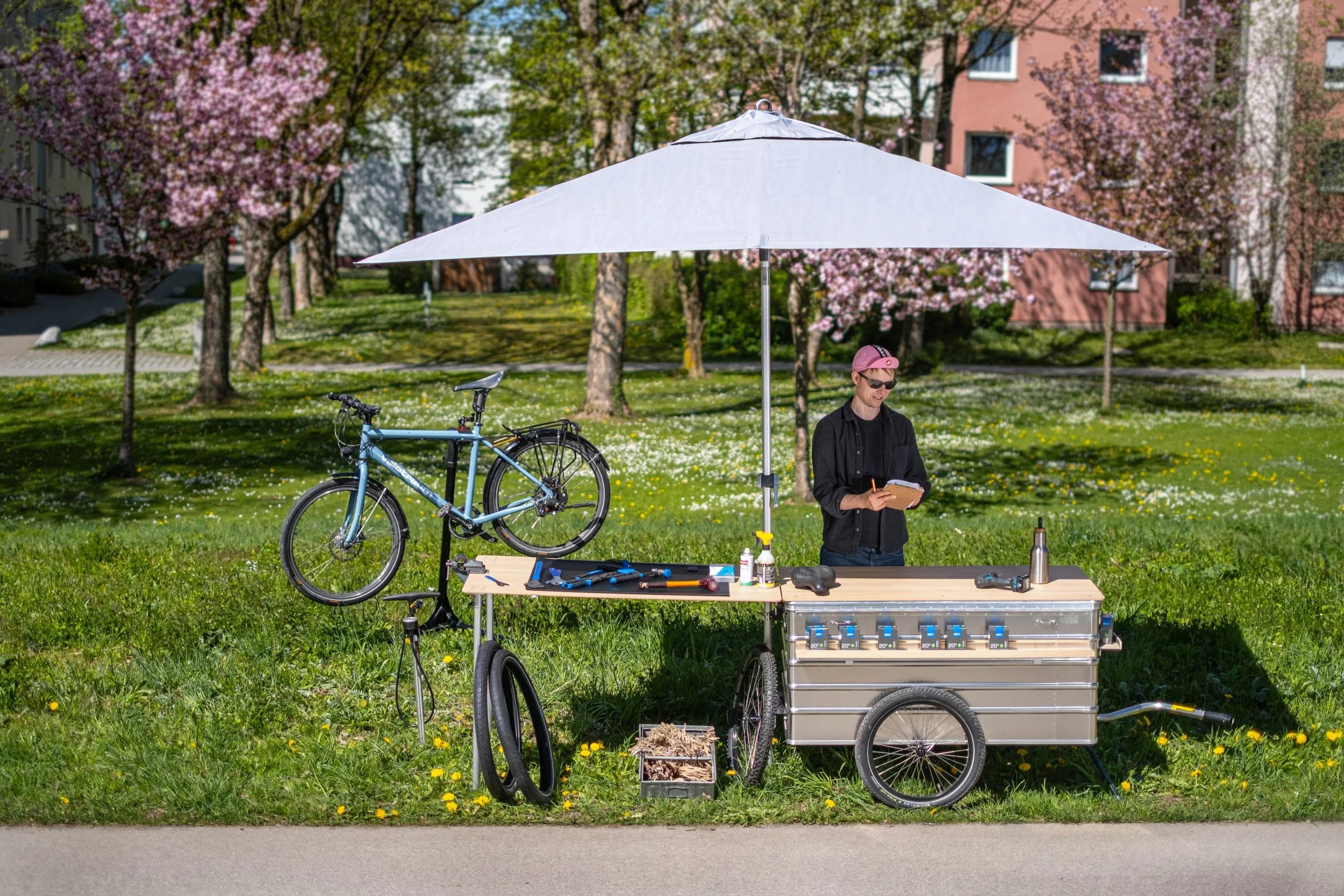Ein mobiler Verkaufsstand, Infostand und Marktstand Fahrradanhänger mit Tischplatte und Schirm als Fahrradreparaturwerkstatt