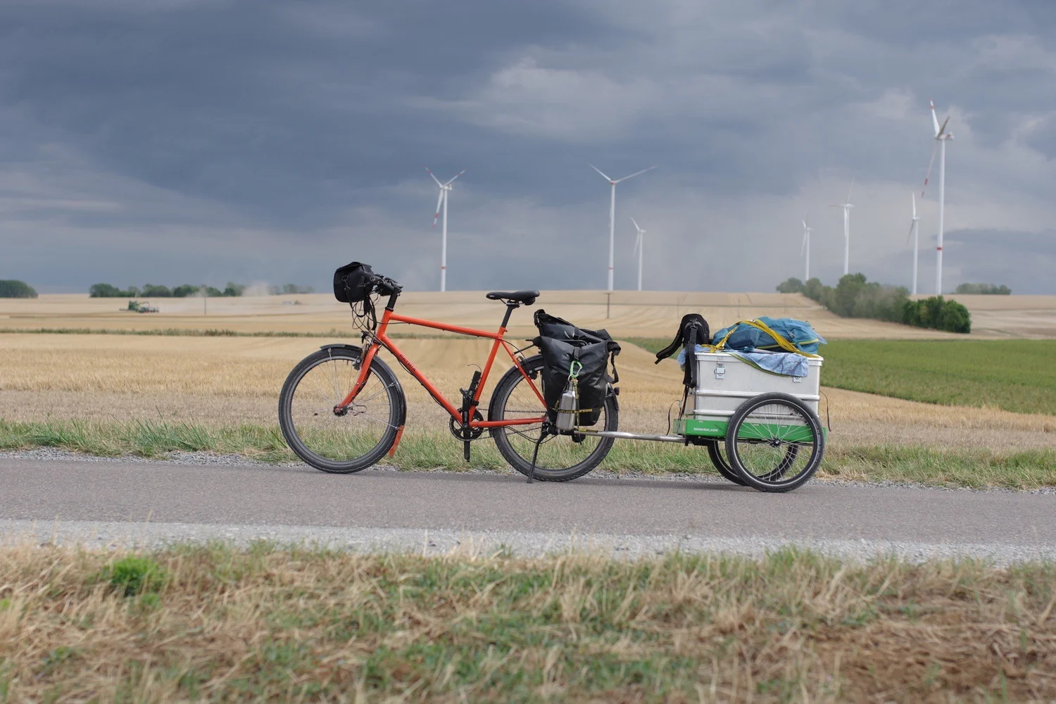 Fahrrad mit Hinterher-Anhänger auf einer Landstraße mit Windrädern
