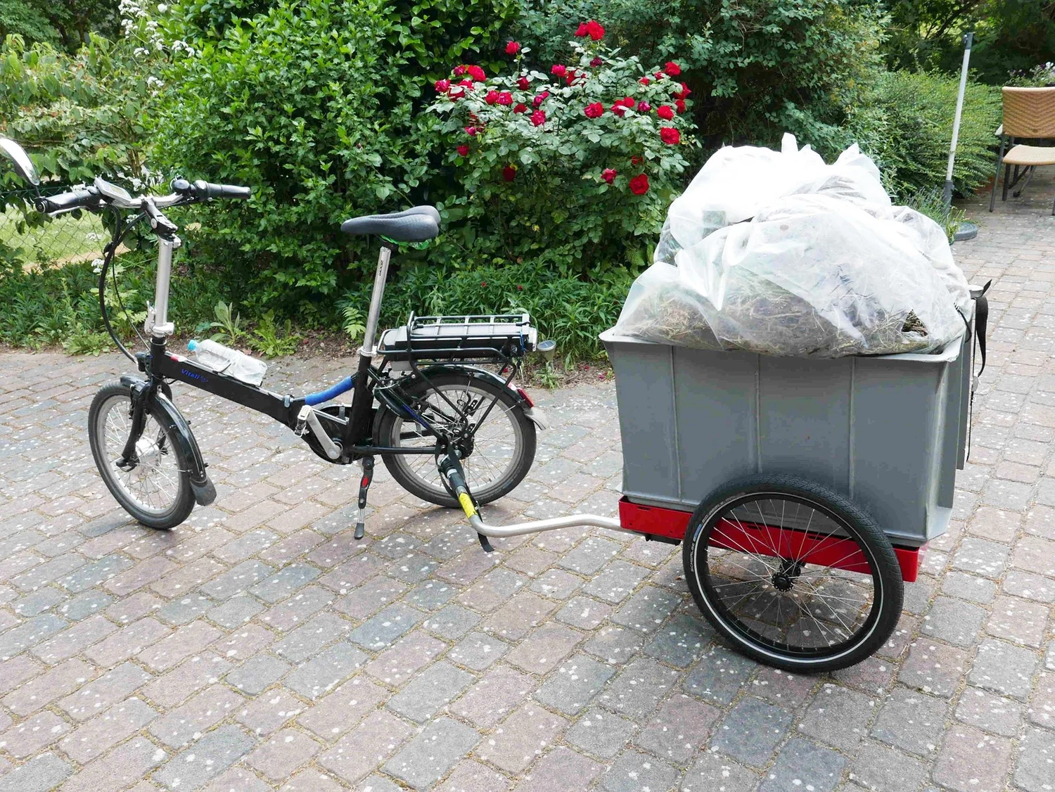 Hinterher Fahrradanhänger mit grauer Eurobox voller Grüngut, dahinter ein Faltrad