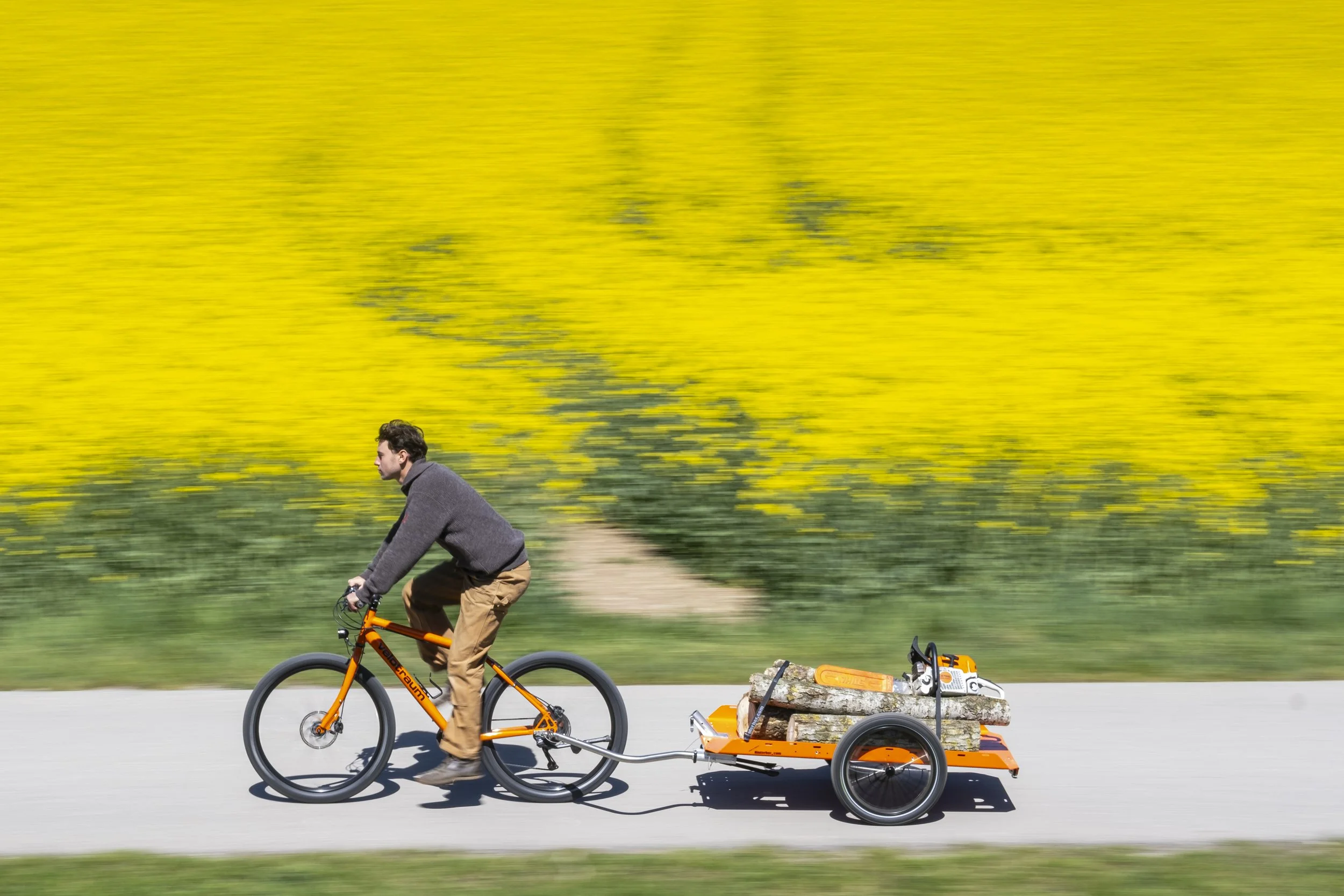 Ein Velotraum Fahrrad zieht einen mit Holz beladenen Transporter Fahrradanhänger des Münchner Herstellers Hinterher