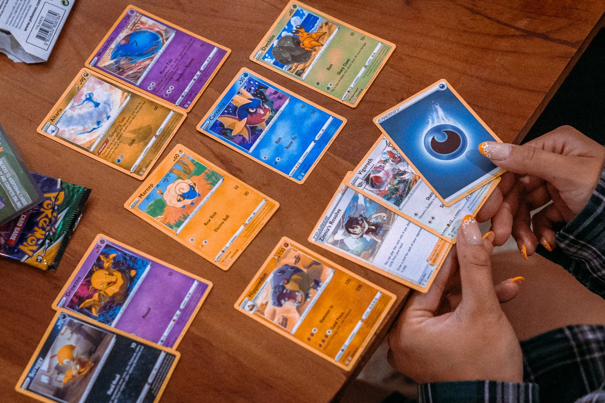 Person playing a Pokémon trading card game with cards laid out on a wooden table.