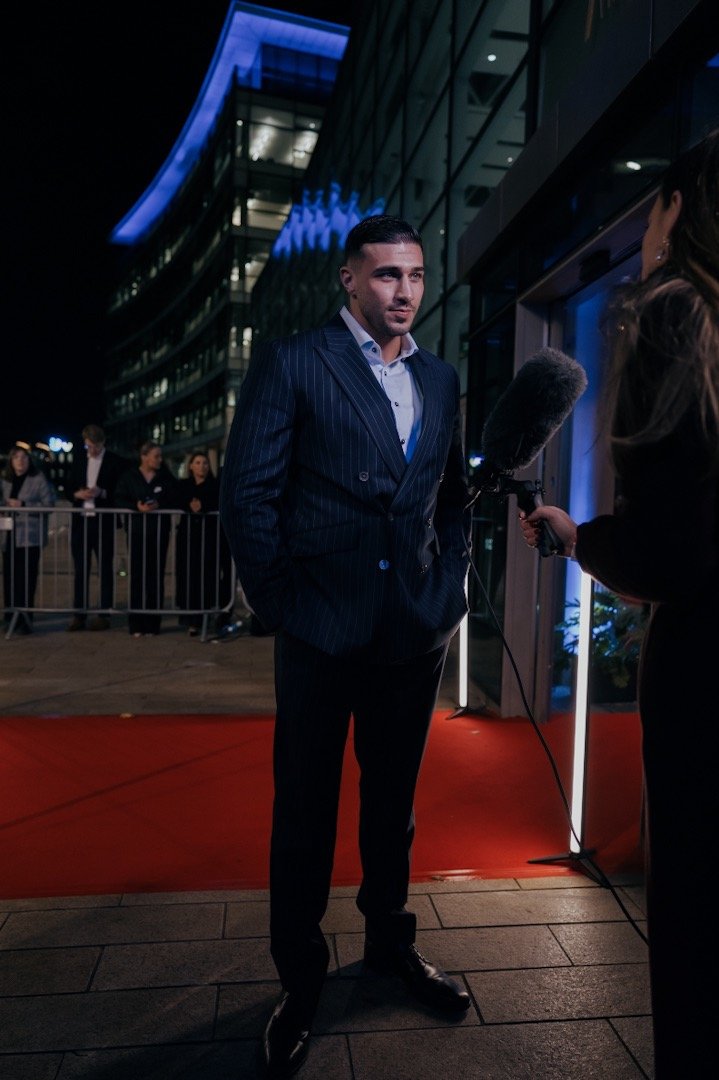 Man in a pinstripe suit being interviewed on a red carpet at night.