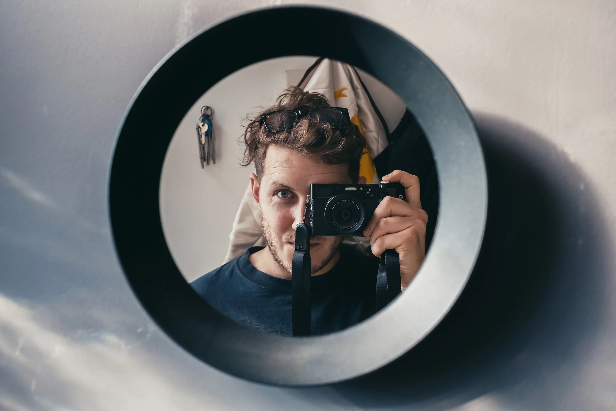 A male looks into a mirror and takes a photo of himself with a dslr camera.