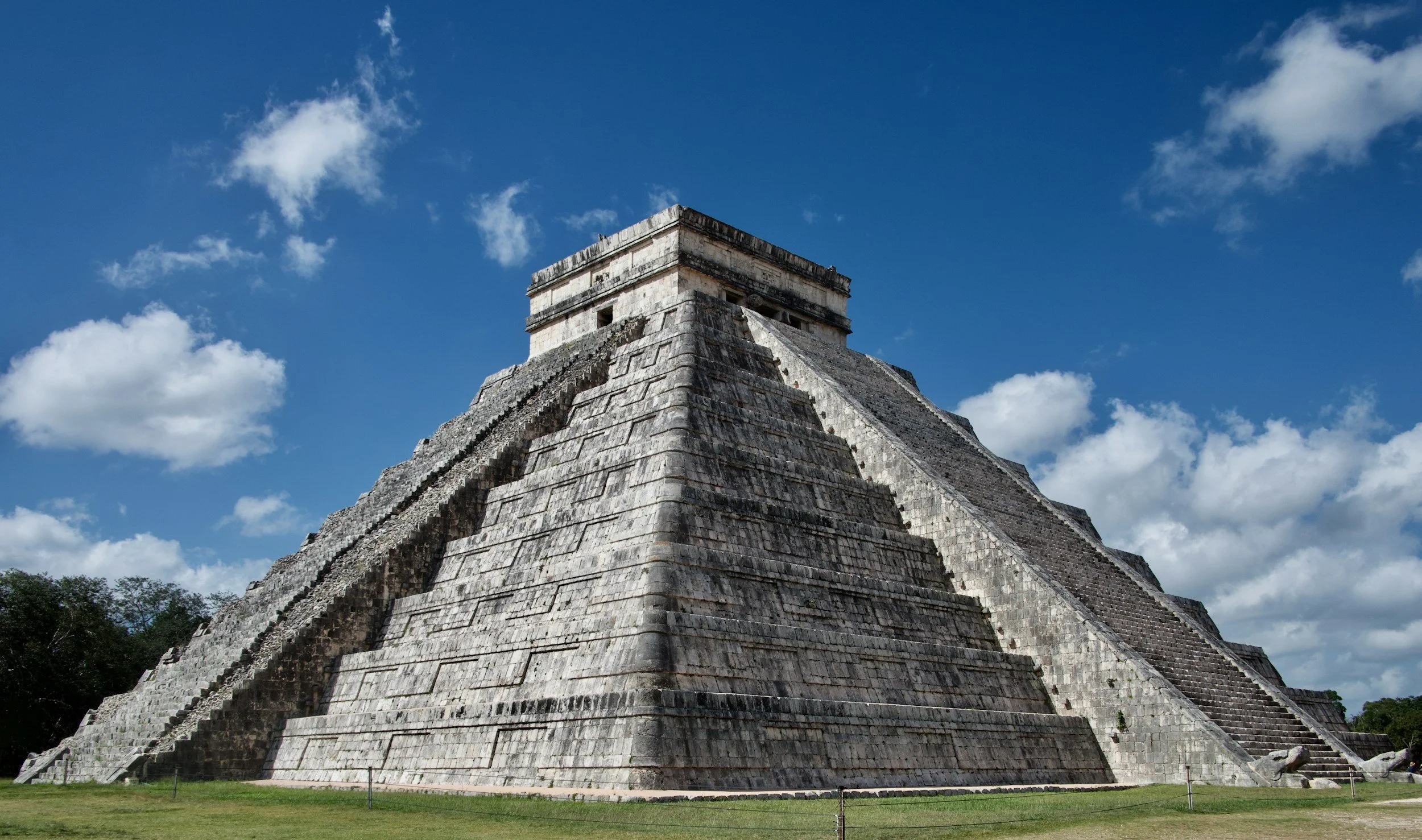 The ancient Mayan pyramid of Kukulcán at Chichen Itza under a partly cloudy sky.