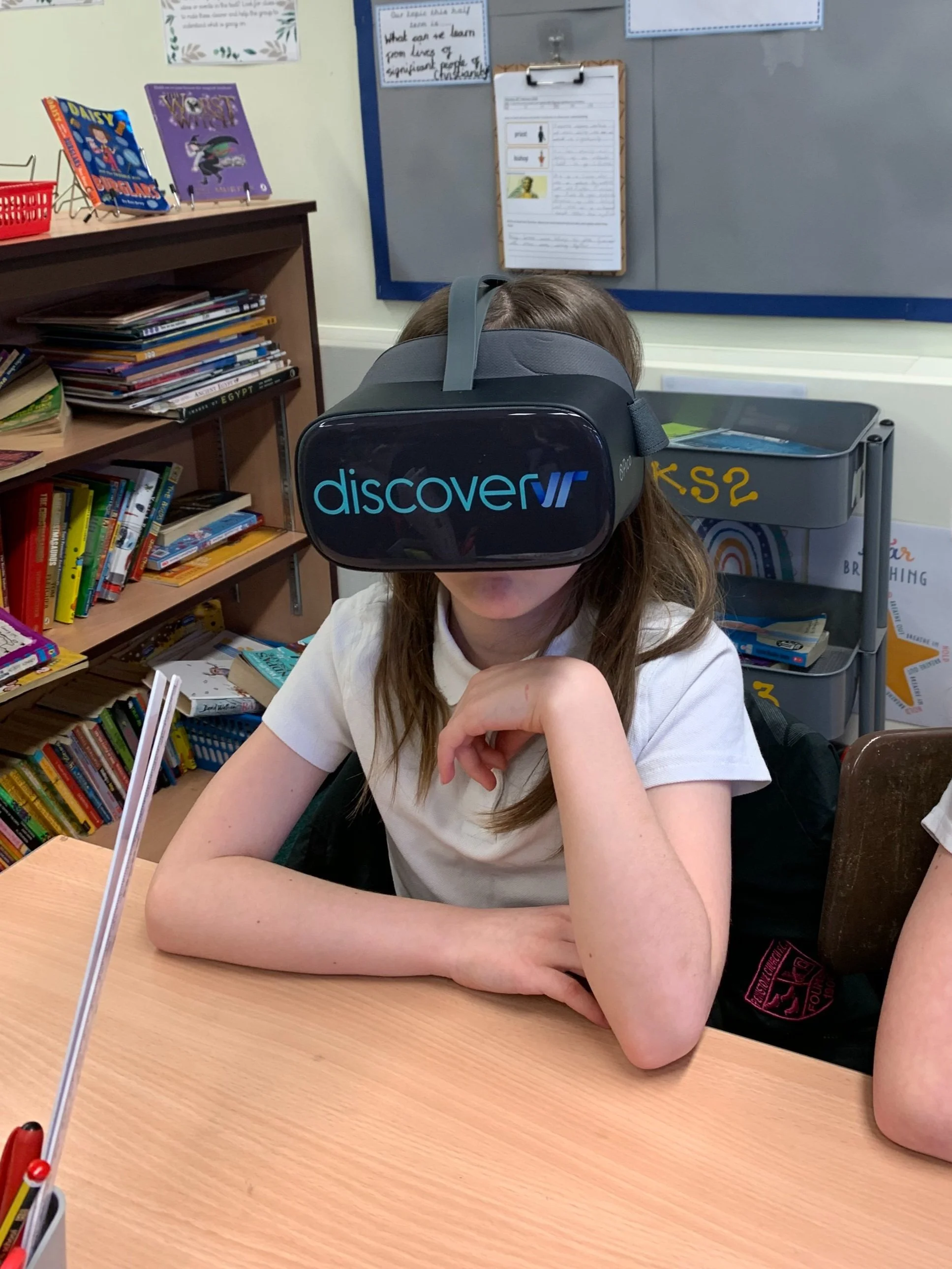 Two children, a boy and a girl, wearing virtual reality headsets while standing in front of a wall decorated with colorful hot air balloon images.
